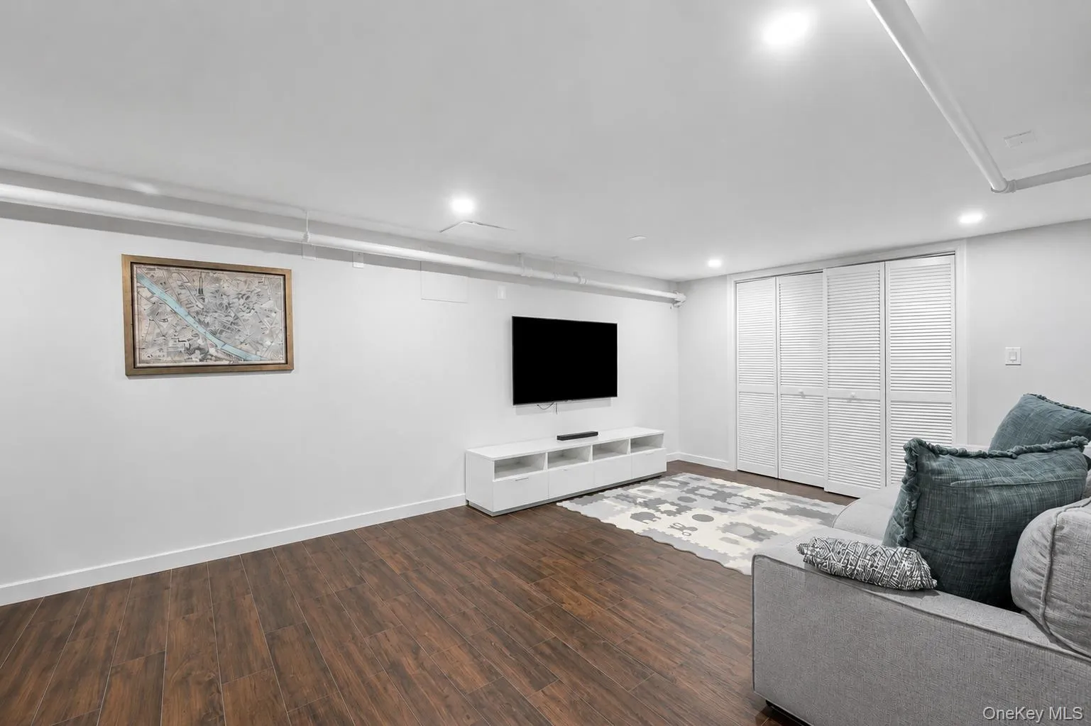 Spacious recreation room in basement with wood-finish flooring, recessed lighting, and white walls Spacious recreation room in basement with wood-finish flooring, recessed lighting, and white walls