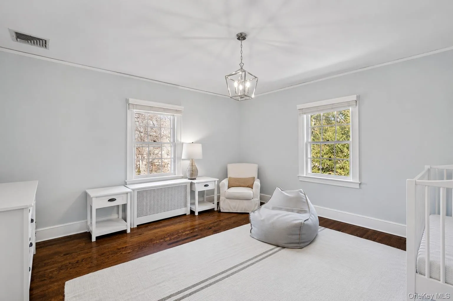 Bright interior featuring two windows, dark wood-finish flooring, and a white baseboard trim Bright interior featuring two windows, dark wood-finish flooring, and a white baseboard trim
