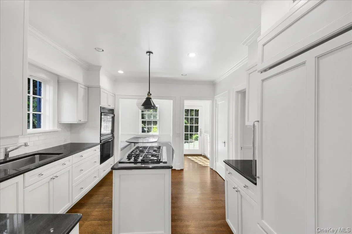 Bright kitchen featuring white cabinetry, dark countertops, a central island with a gas cooktop, built-in oven, and paneled refrigerator Bright kitchen featuring white cabinetry, dark countertops, a central island with a gas cooktop, built-in oven, and paneled refrigerator