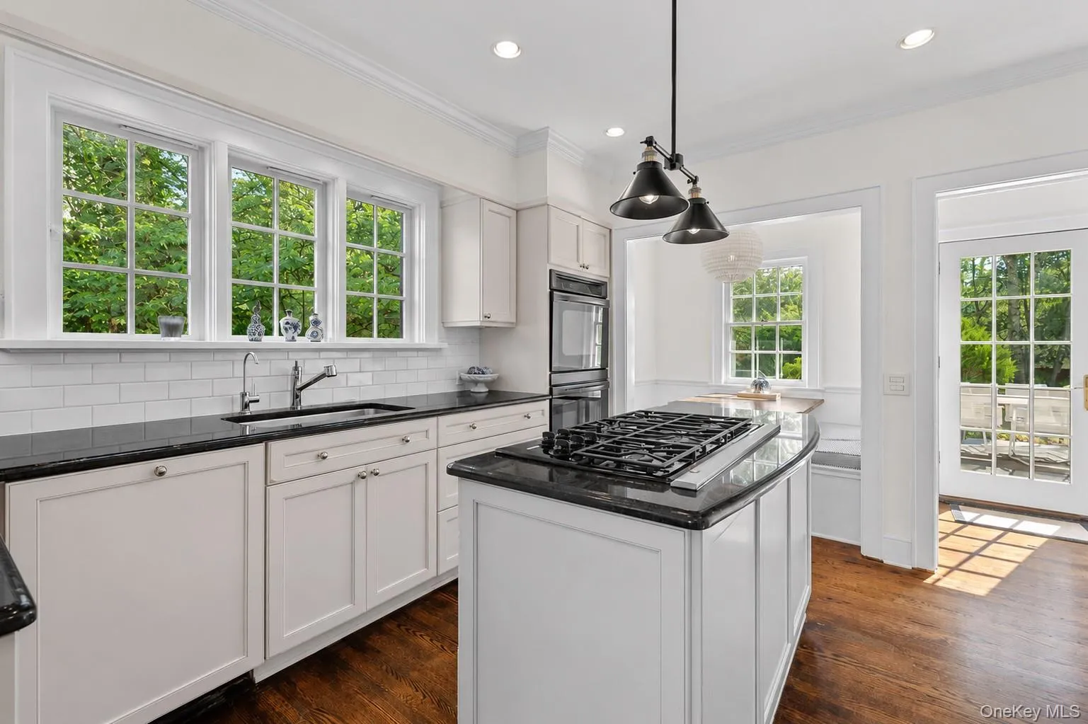 Kitchen featuring a center island with a gas cooktop, white cabinetry, dark countertops, built-in double ovens, and wood-finish flooring Kitchen featuring a center island with a gas cooktop, white cabinetry, dark countertops, built-in double ovens, and wood-finish flooring