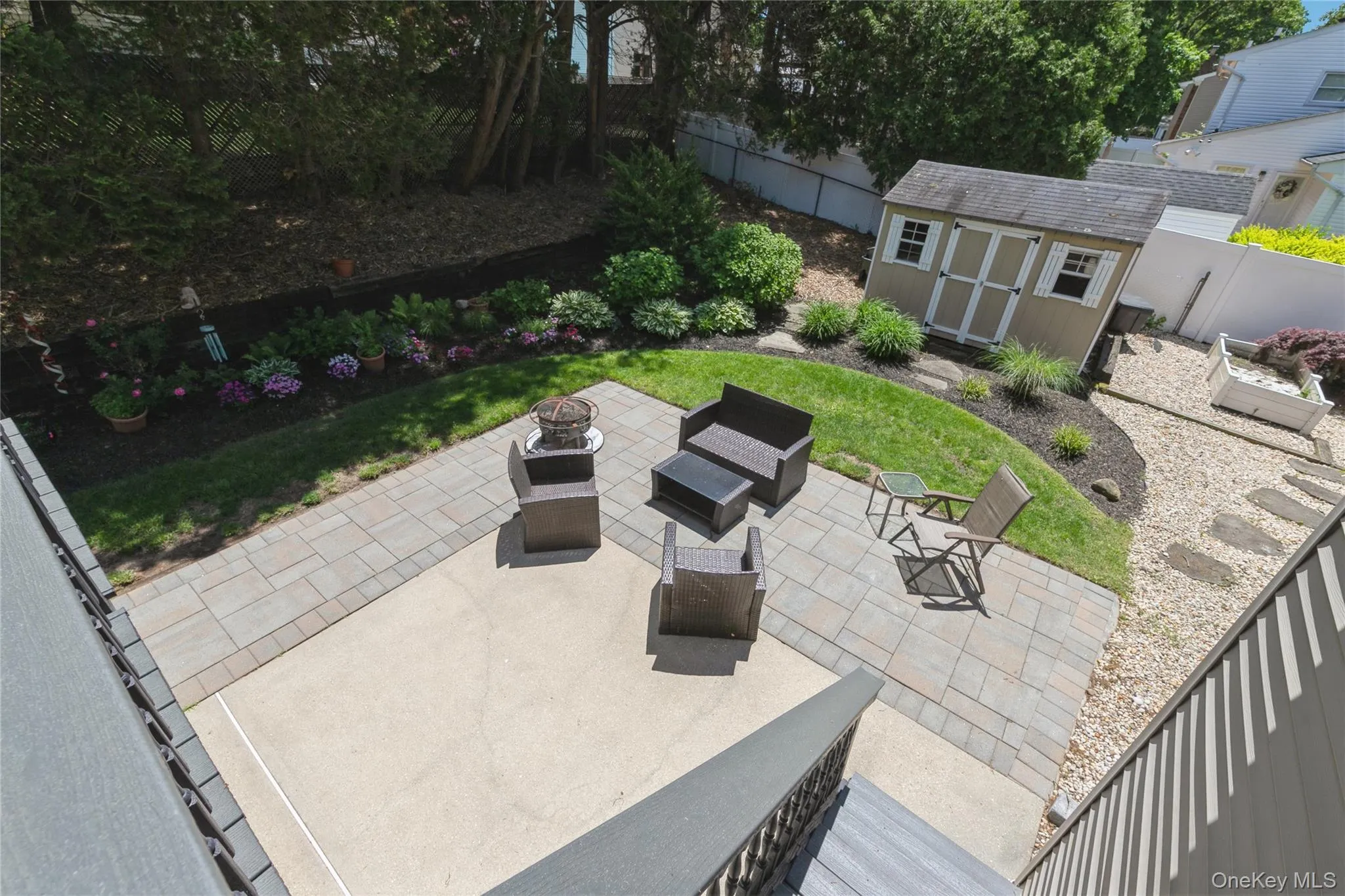 Expansive backyard featuring a paver patio with a concrete section, manicured lawn, and a storage shed with white window shutters Expansive backyard featuring a paver patio with a concrete section, manicured lawn, and a storage shed with white window shutters