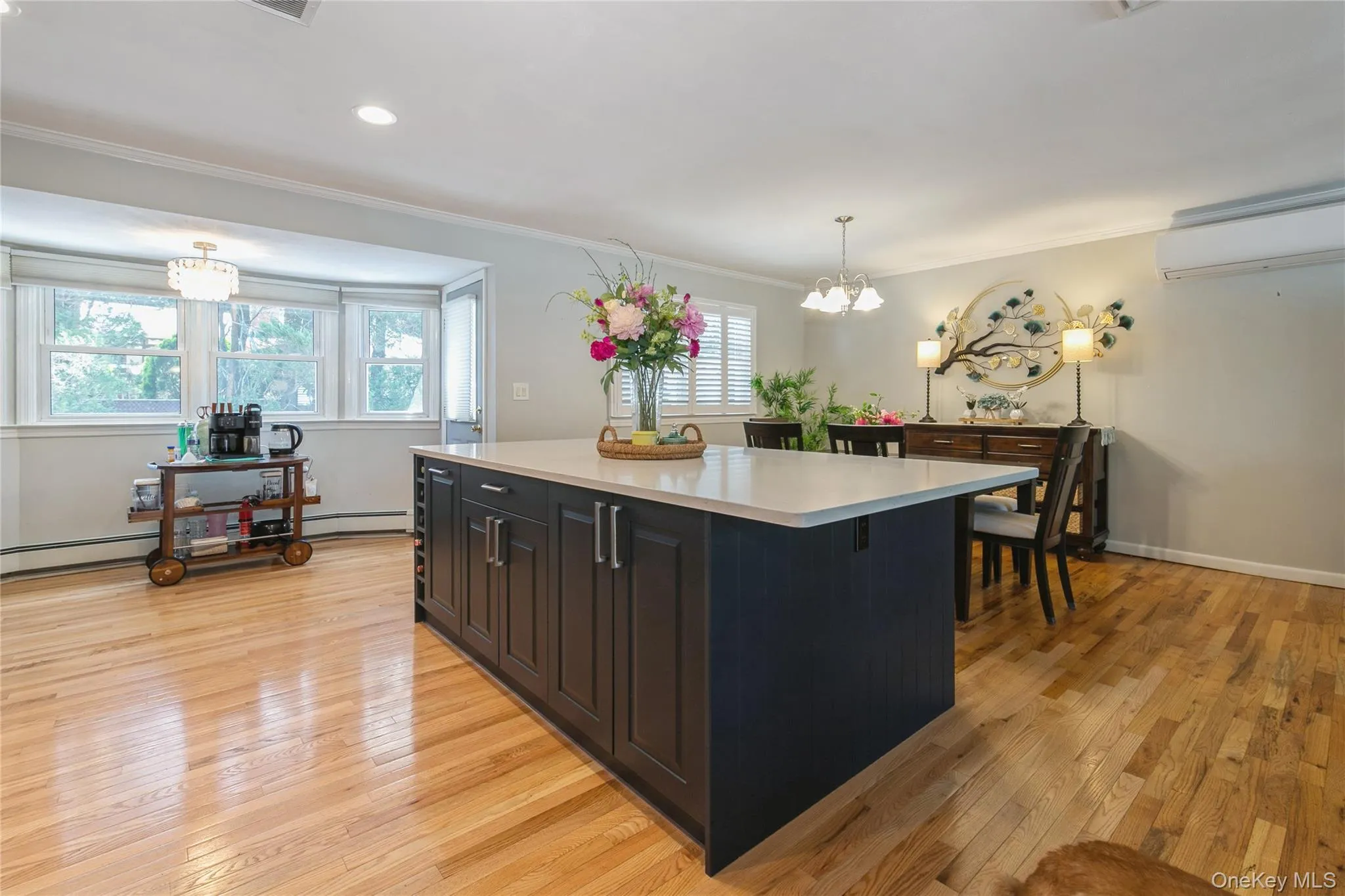 Kitchen island with dark cabinetry and light-toned countertop, featuring wood-finish flooring throughout Kitchen island with dark cabinetry and light-toned countertop, featuring wood-finish flooring throughout