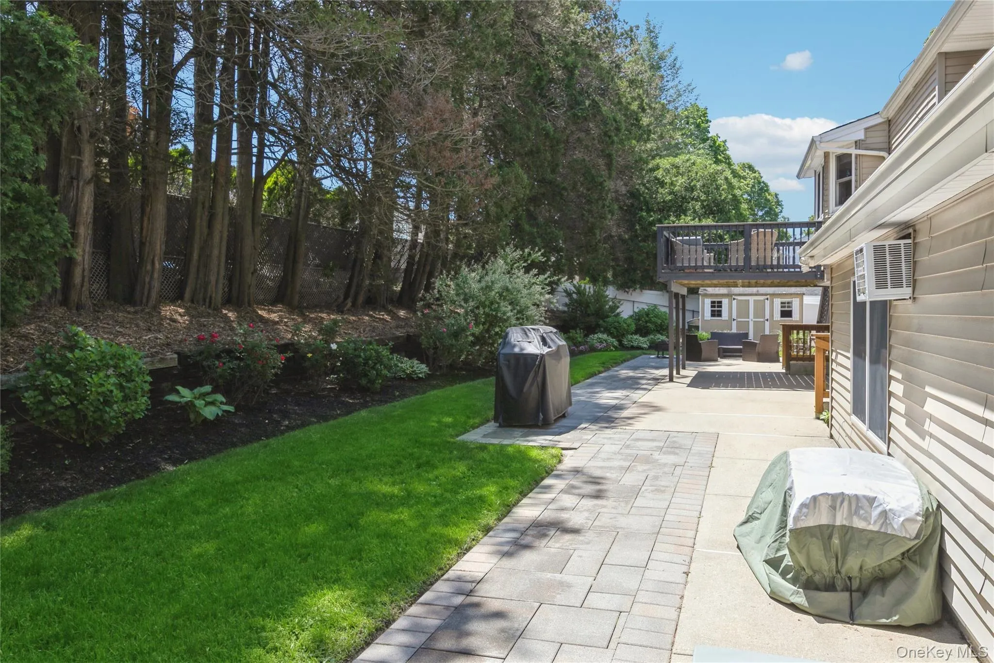 Expansive backyard featuring a paver stone pathway, a manicured lawn, and mature perimeter trees Expansive backyard featuring a paver stone pathway, a manicured lawn, and mature perimeter trees