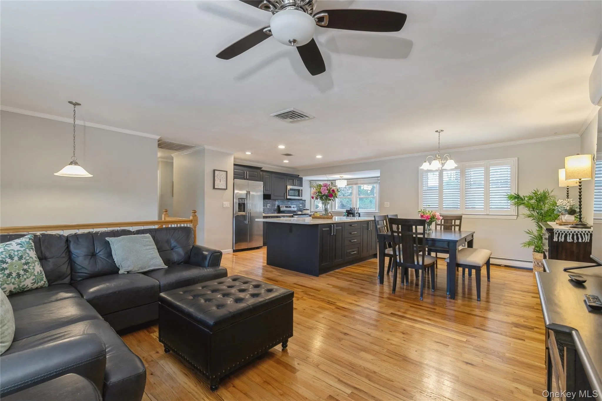 Open-concept living space featuring wood-finish flooring, a ceiling fan with light fixture, and a kitchen island with seating Open-concept living space featuring wood-finish flooring, a ceiling fan with light fixture, and a kitchen island with seating