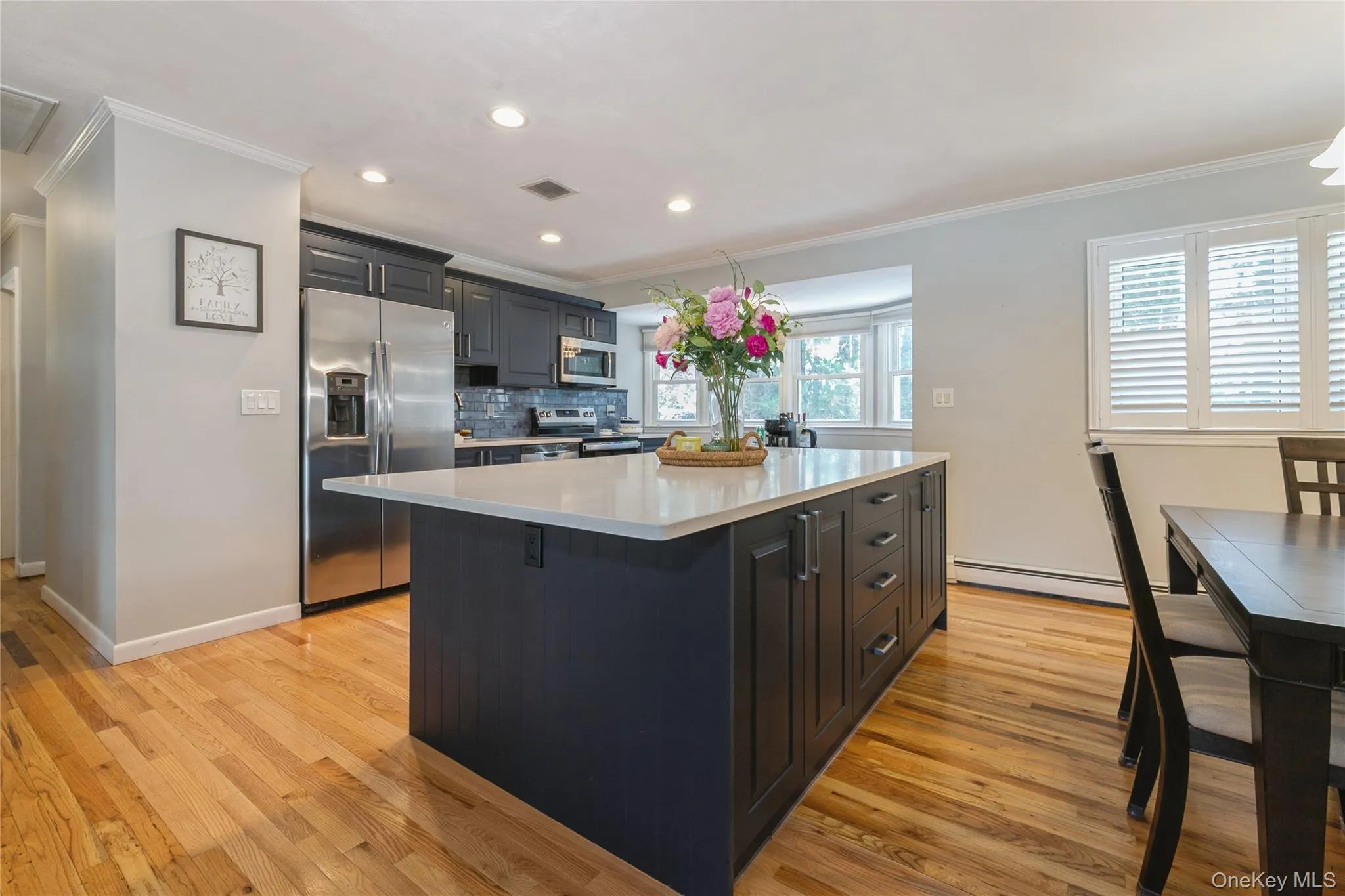 Kitchen featuring a dark-toned island with storage, light countertop, stainless steel appliances, and wood-finish flooring Kitchen featuring a dark-toned island with storage, light countertop, stainless steel appliances, and wood-finish flooring