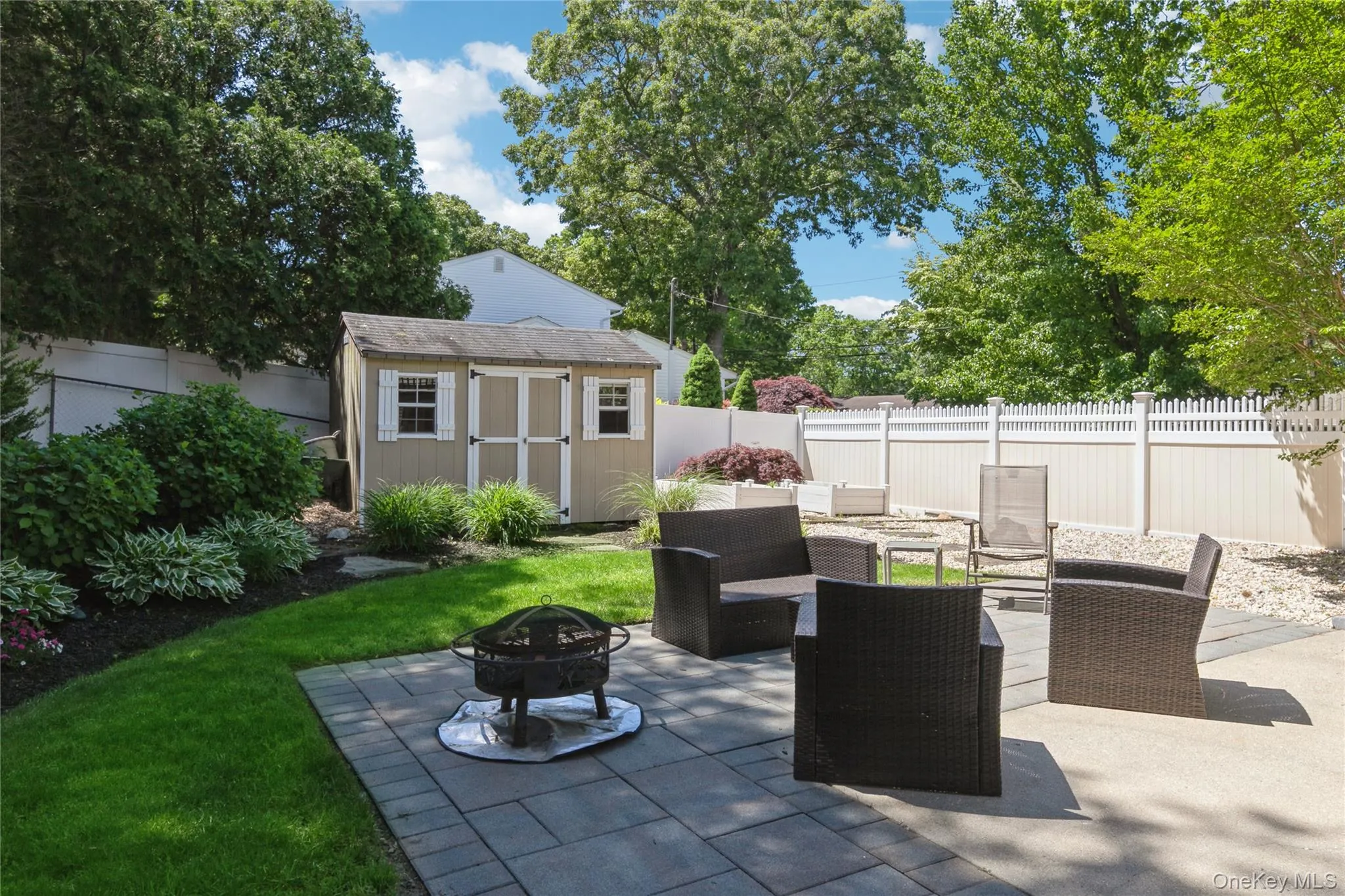 Paved patio area, manicured lawn, landscaping with mature shrubs, privacy fencing, and a detached shed with double doors Paved patio area, manicured lawn, landscaping with mature shrubs, privacy fencing, and a detached shed with double doors