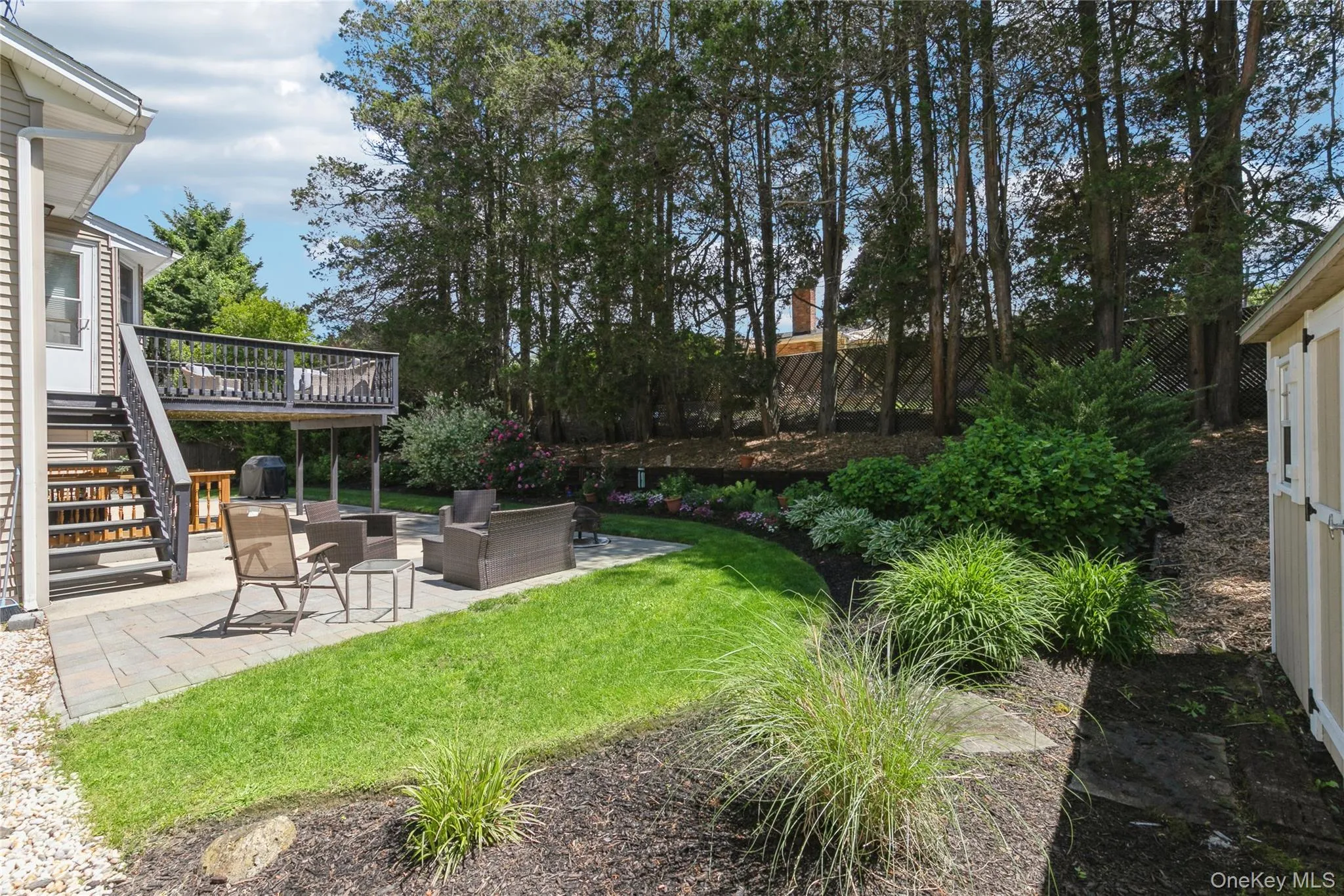 Backyard featuring a paver patio, lush lawn, elevated wood deck with stairs, landscaped planting beds, and a storage shed Backyard featuring a paver patio, lush lawn, elevated wood deck with stairs, landscaped planting beds, and a storage shed