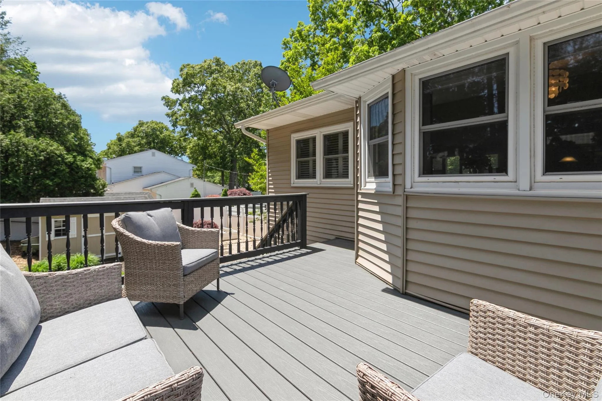 Expansive composite deck featuring a dark railing, tan siding, and multiple windows Expansive composite deck featuring a dark railing, tan siding, and multiple windows