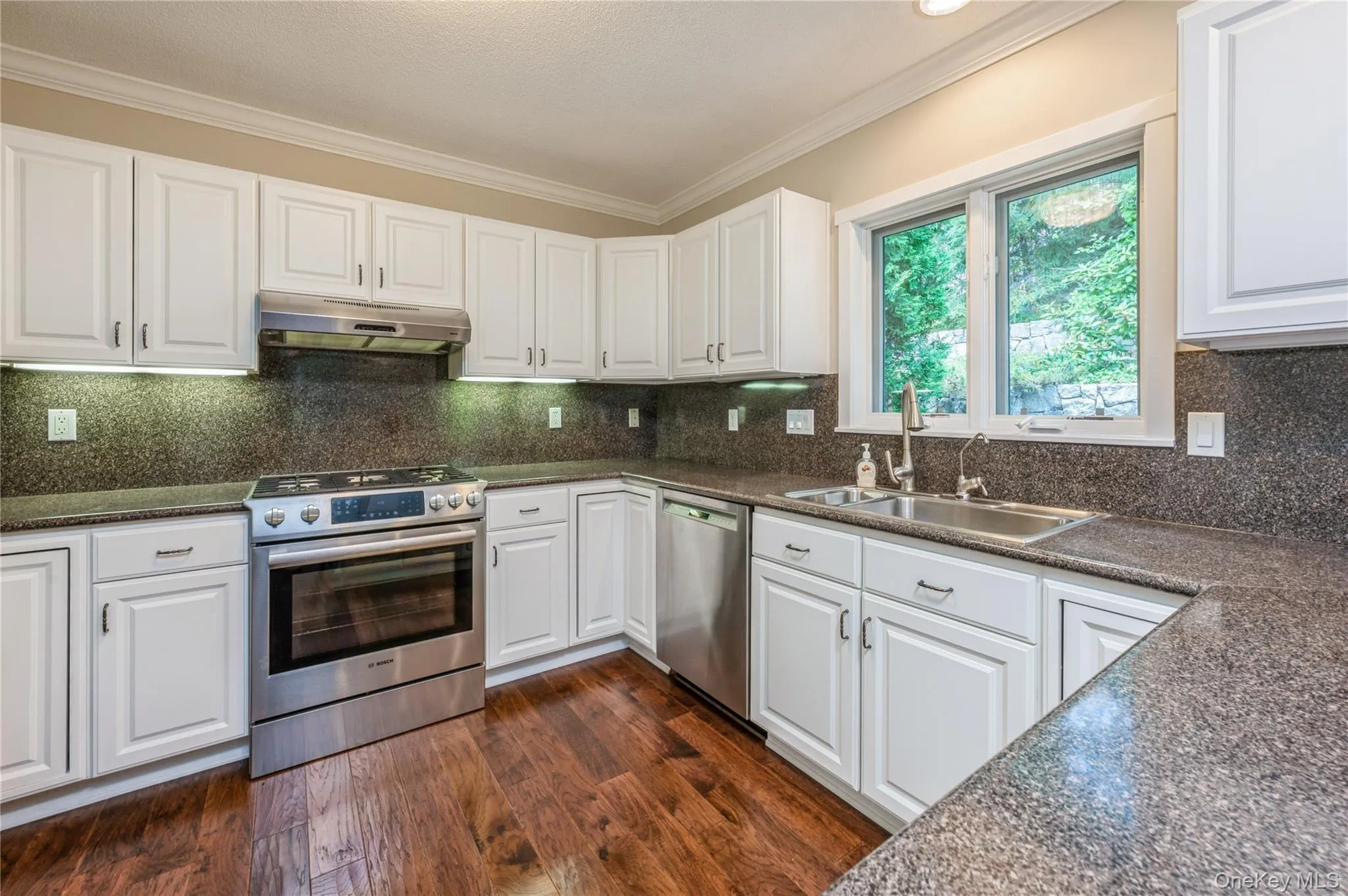 Kitchen with stainless steel appliances, under cabinet range hood, dark countertops, crown molding, and white cabinets Kitchen with stainless steel appliances, under cabinet range hood, dark countertops, crown molding, and white cabinets