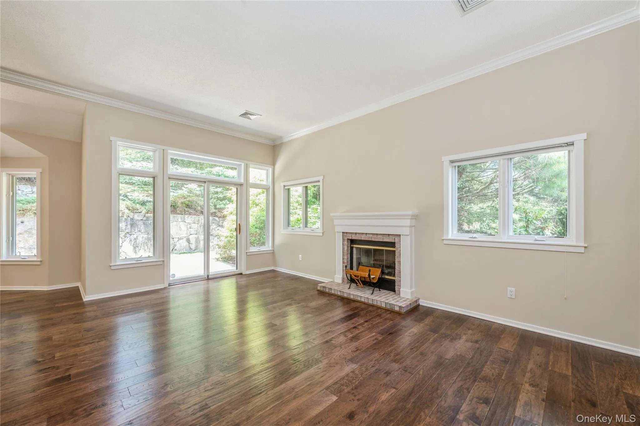 Unfurnished living room with a brick fireplace, dark wood finished floors, and ornamental molding Unfurnished living room with a brick fireplace, dark wood finished floors, and ornamental molding