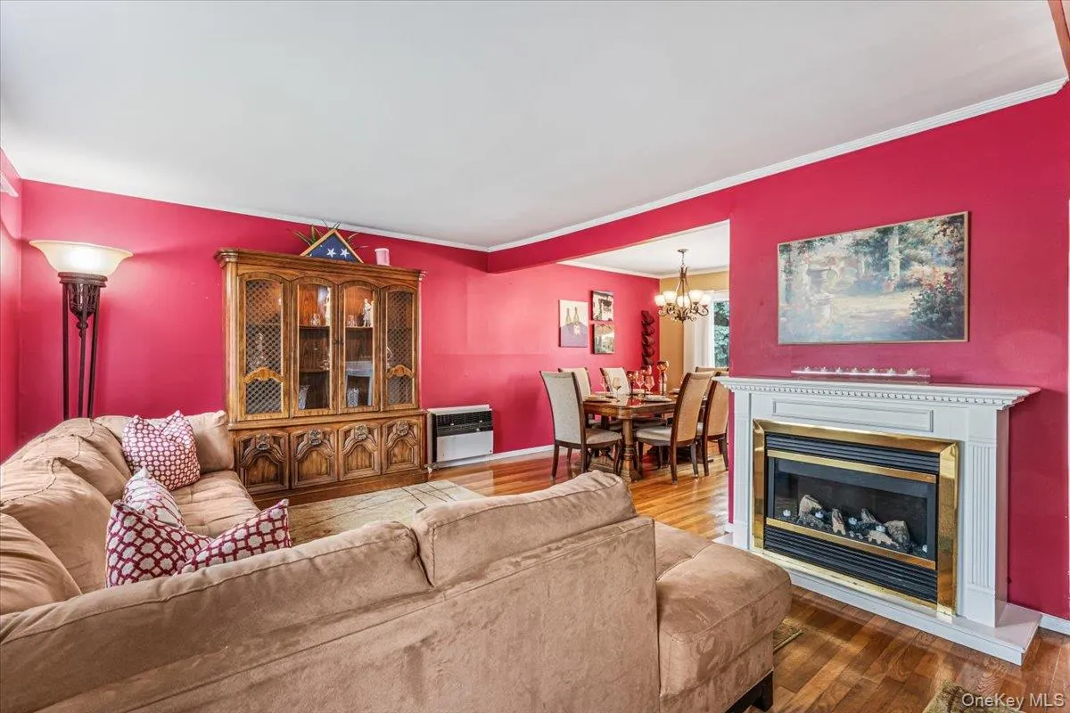 Living area featuring wood-finish flooring, a white mantel, and a electric fireplace with a brass-tone trim Living area featuring wood-finish flooring, a white mantel, and a electric fireplace with a brass-tone trim