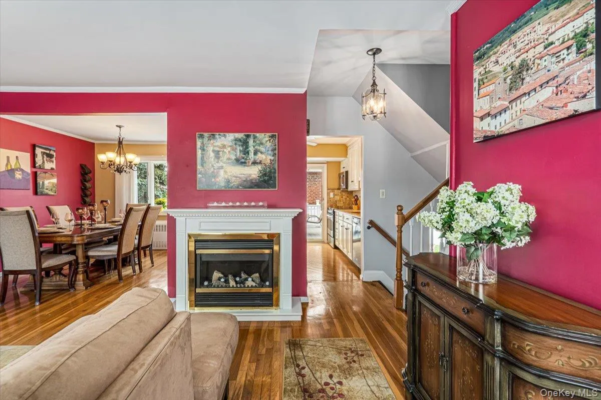 Living area featuring a white mantel electric fireplace with a gold-toned insert, wood-finish flooring, and crown molding Living area featuring a white mantel electric fireplace with a gold-toned insert, wood-finish flooring, and crown molding