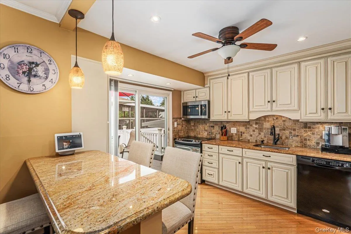 Kitchen featuring an eat-at countertop, cream cabinetry, a tile backsplash, and a sliding glass door to an outdoor deck Kitchen featuring an eat-at countertop, cream cabinetry, a tile backsplash, and a sliding glass door to an outdoor deck