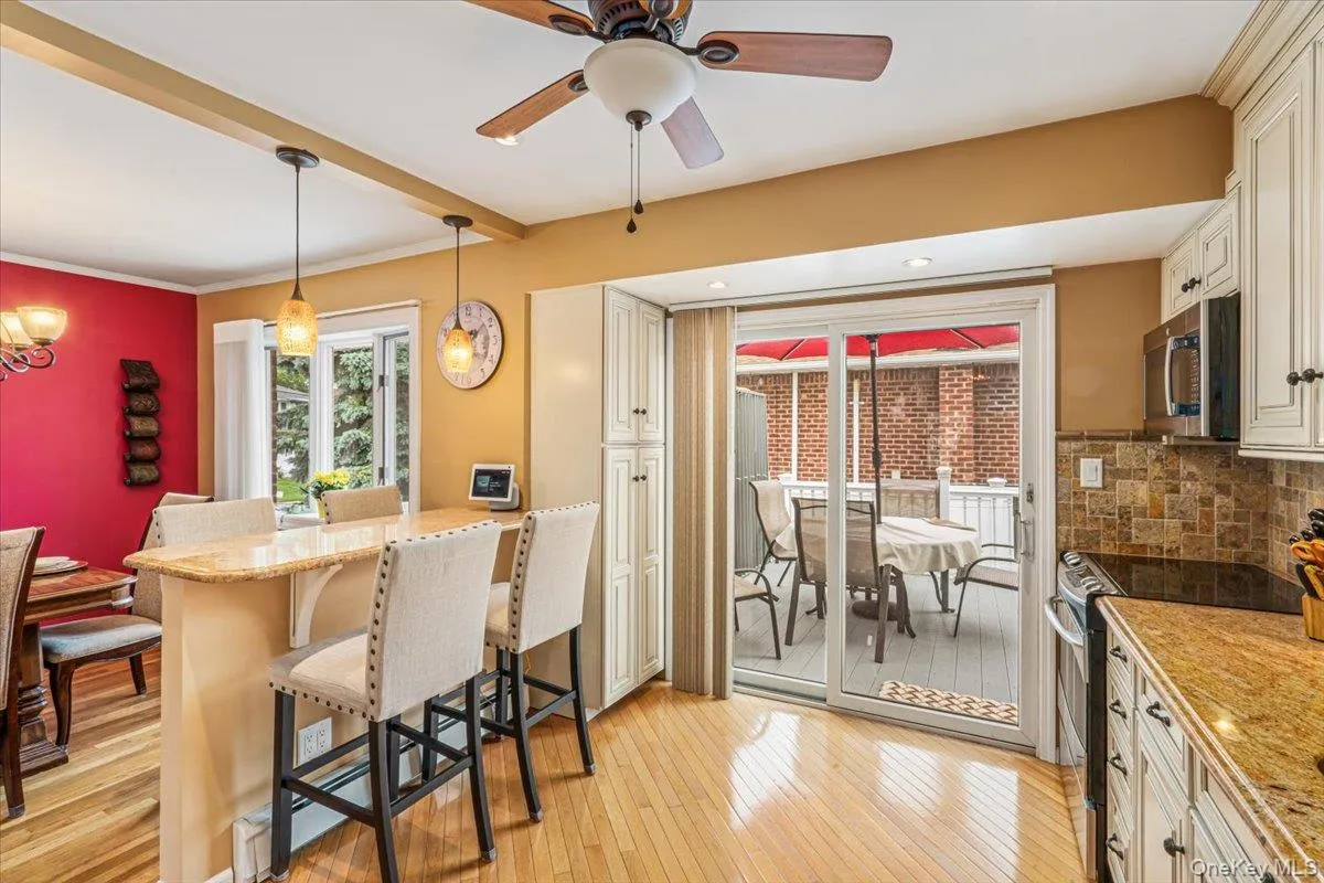 Kitchen space featuring light wood-finish flooring, a built-in breakfast bar with pendant lighting, white cabinetry, stainless steel appliances, and a tiled backsplash Kitchen space featuring light wood-finish flooring, a built-in breakfast bar with pendant lighting, white cabinetry, stainless steel appliances, and a tiled backsplash