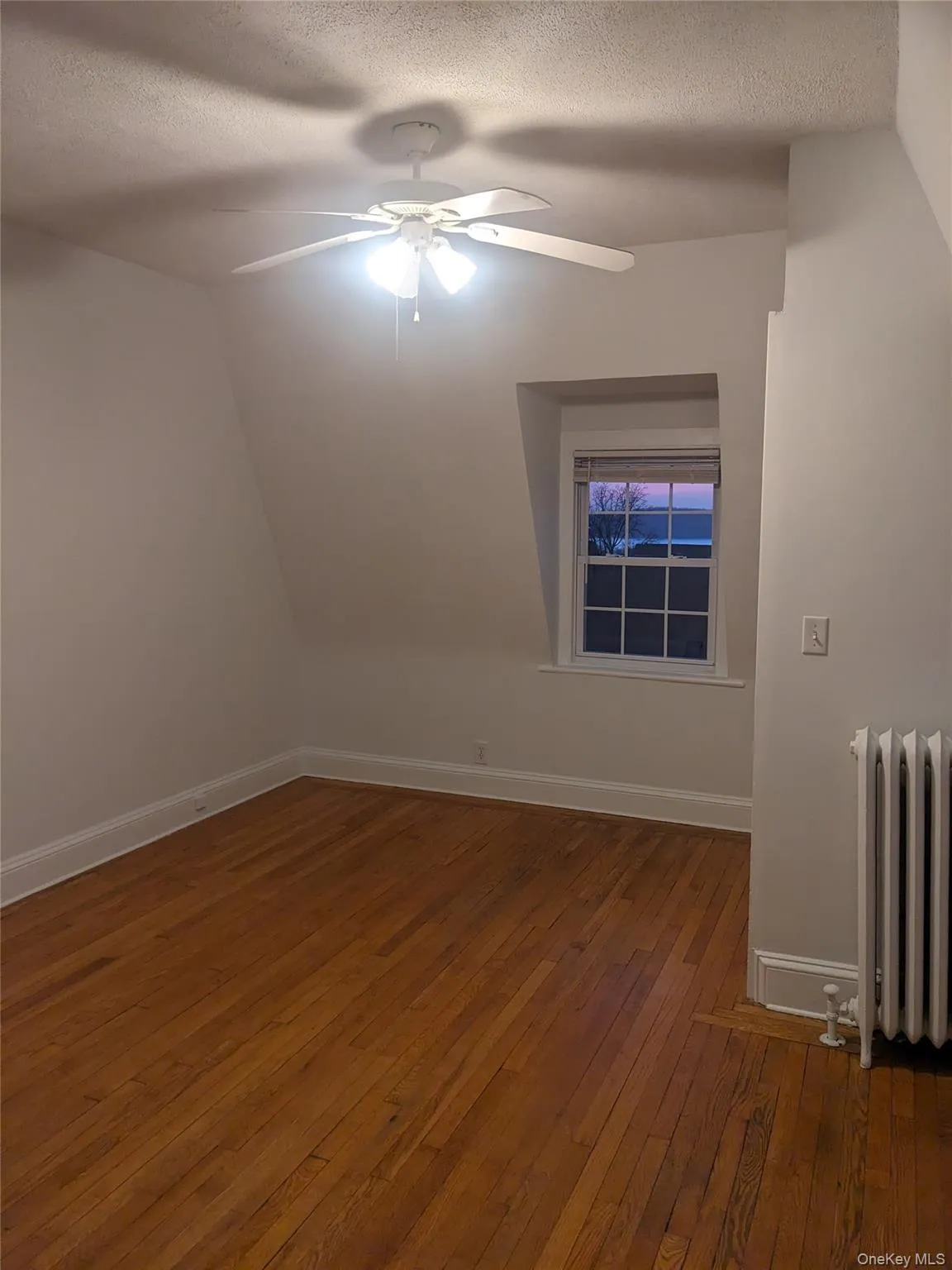 Additional living space with hardwood / wood-style flooring, a ceiling fan, a textured ceiling, radiator, and baseboards Additional living space with hardwood / wood-style flooring, a ceiling fan, a textured ceiling, radiator, and baseboards