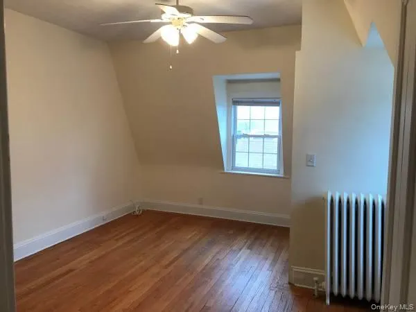 Additional living space with radiator, wood finished floors, ceiling fan, and baseboards Additional living space with radiator, wood finished floors, ceiling fan, and baseboards