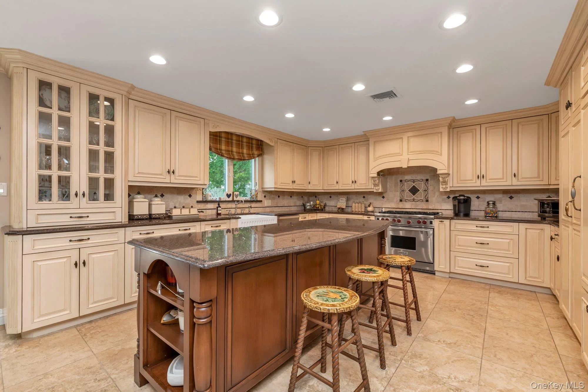 Expansive kitchen featuring a large central island with storage, extensive cream-colored cabinetry, tile flooring, a professional-grade range, and recessed lighting Expansive kitchen featuring a large central island with storage, extensive cream-colored cabinetry, tile flooring, a professional-grade range, and recessed lighting