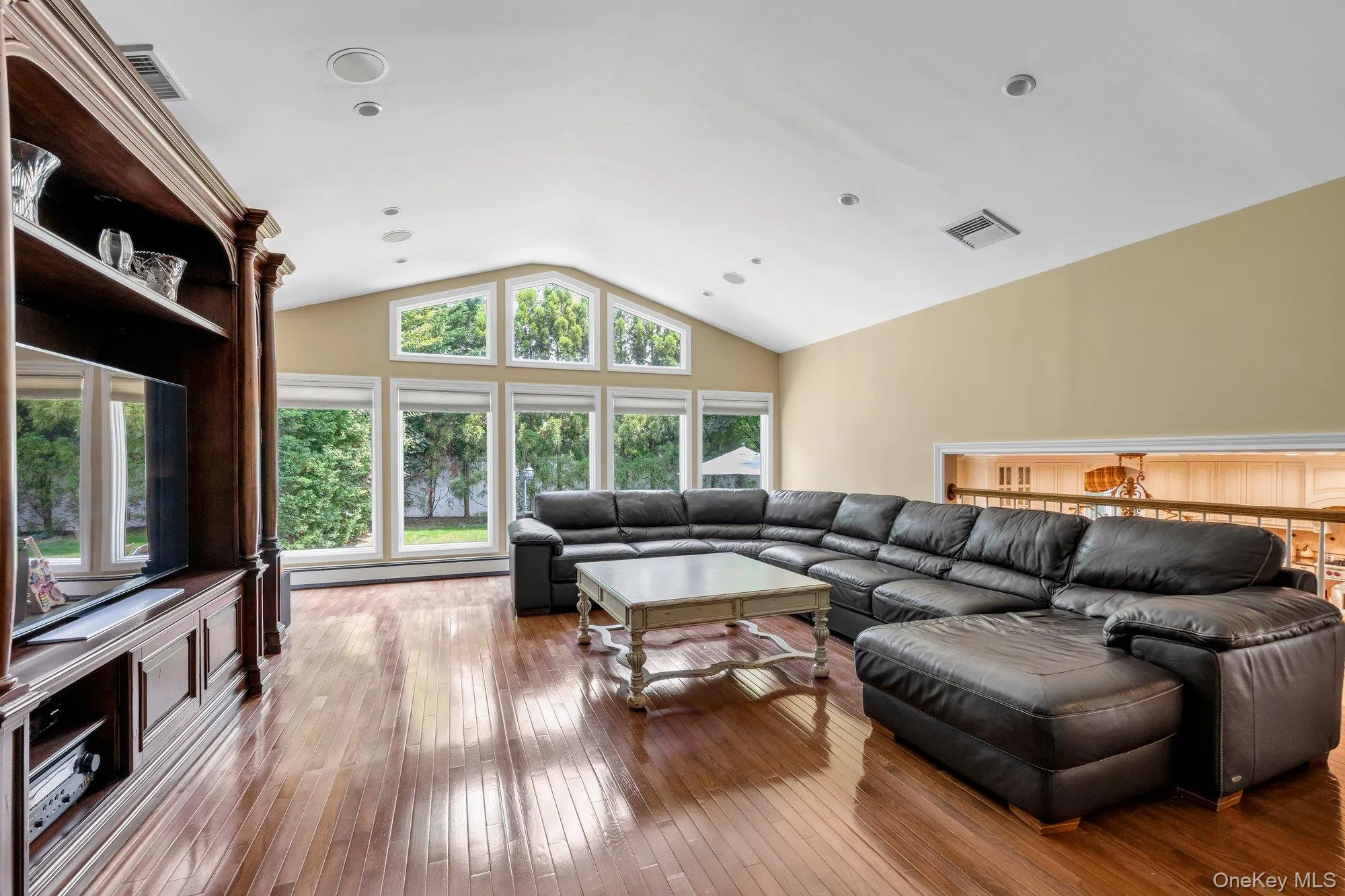 Vaulted ceiling expanded den featuring extensive natural light from a full wall of windows, rich wood-finish flooring, a built-in entertainment center, and integrated ceiling speakers Vaulted ceiling expanded den featuring extensive natural light from a full wall of windows, rich wood-finish flooring, a built-in entertainment center, and integrated ceiling speakers