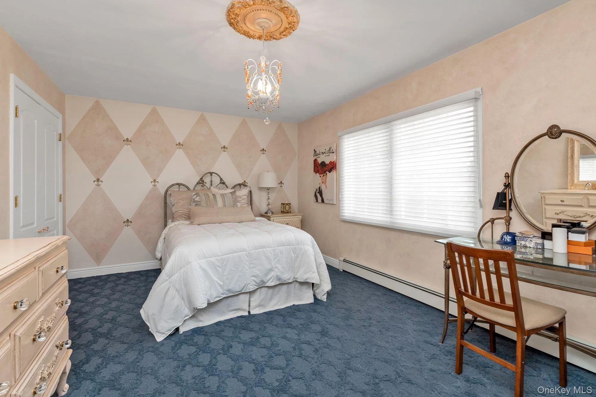 Bedroom featuring a decorative accent wall, a large window with blinds, blue patterned carpet, a built-in closet with double doors, and an ornate ceiling medallion with a chandelier Bedroom featuring a decorative accent wall, a large window with blinds, blue patterned carpet, a built-in closet with double doors, and an ornate ceiling medallion with a chandelier