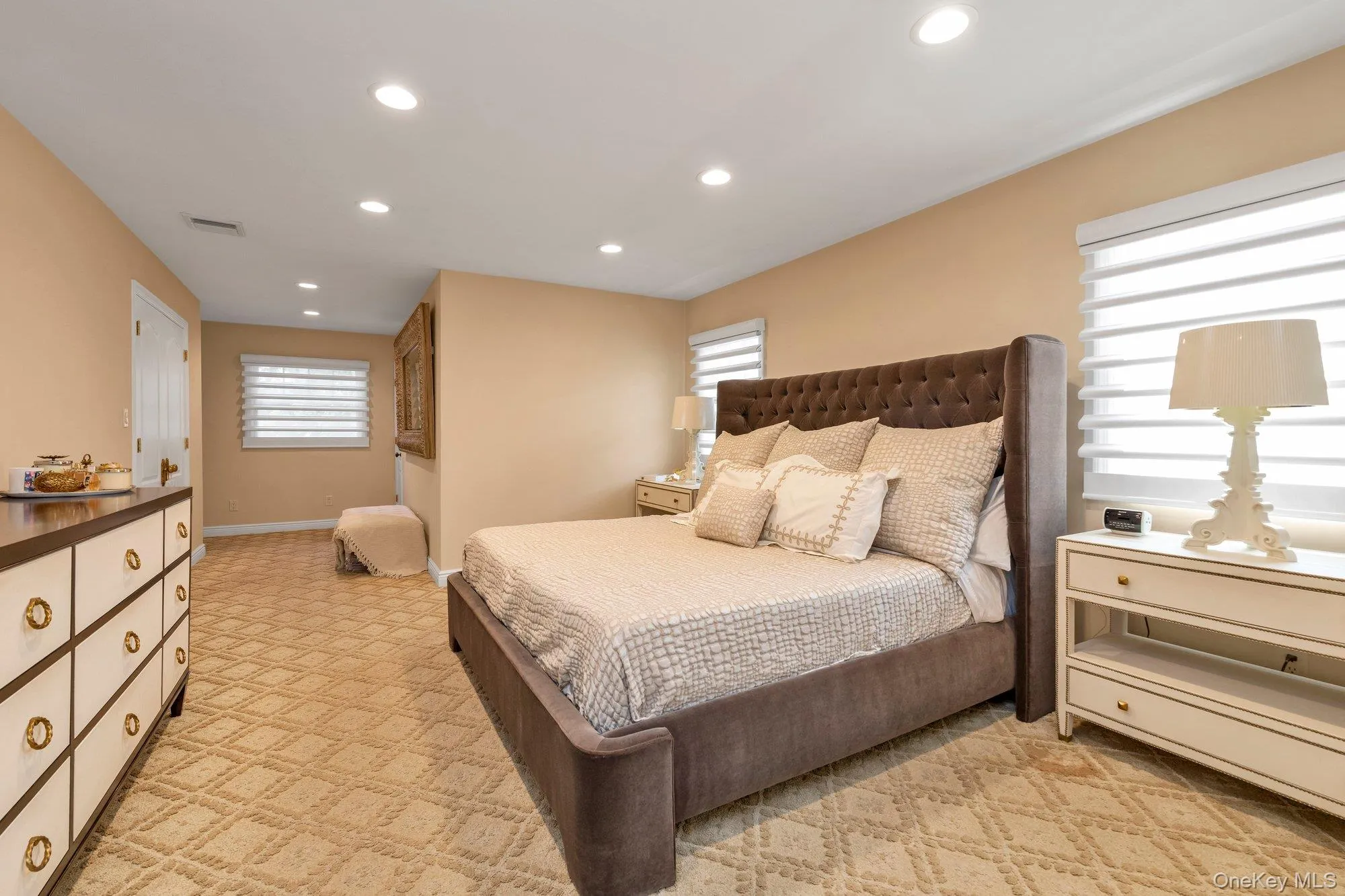 Large primary suite with wall-to-wall patterned carpeting, recessed ceiling lighting, and multiple windows with horizontal blinds, has a big closet Large primary suite with wall-to-wall patterned carpeting, recessed ceiling lighting, and multiple windows with horizontal blinds, has a big closet