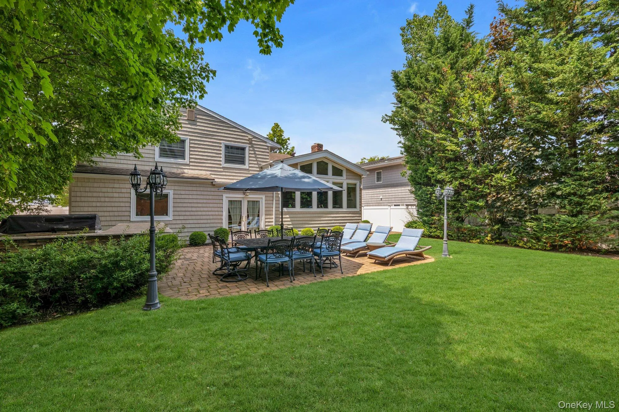 Expansive rear yard featuring a brick paver patio, with multiple windows, and a manicured lawn Expansive rear yard featuring a brick paver patio, with multiple windows, and a manicured lawn
