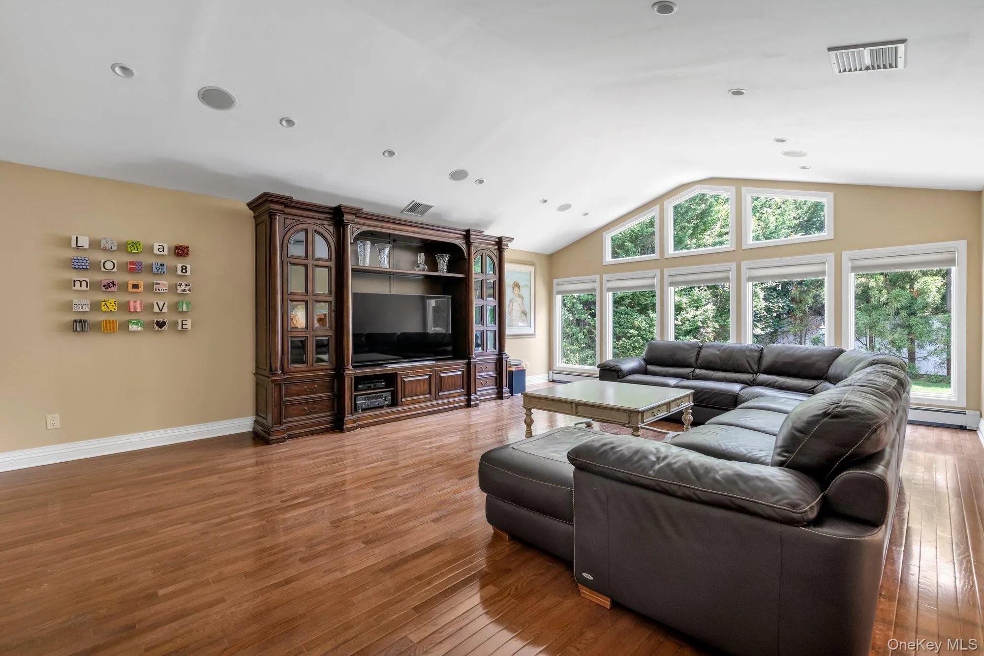 Spacious expanded den/living area featuring wood-finish flooring, a vaulted ceiling, recessed lighting, and a wall of windows Spacious expanded den/living area featuring wood-finish flooring, a vaulted ceiling, recessed lighting, and a wall of windows