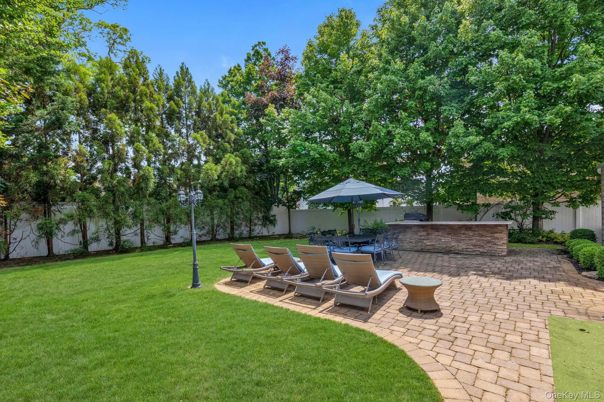 Expansive backyard featuring a stone paver patio, a built-in stacked stone outdoor bar, mature trees, and a manicured lawn Expansive backyard featuring a stone paver patio, a built-in stacked stone outdoor bar, mature trees, and a manicured lawn