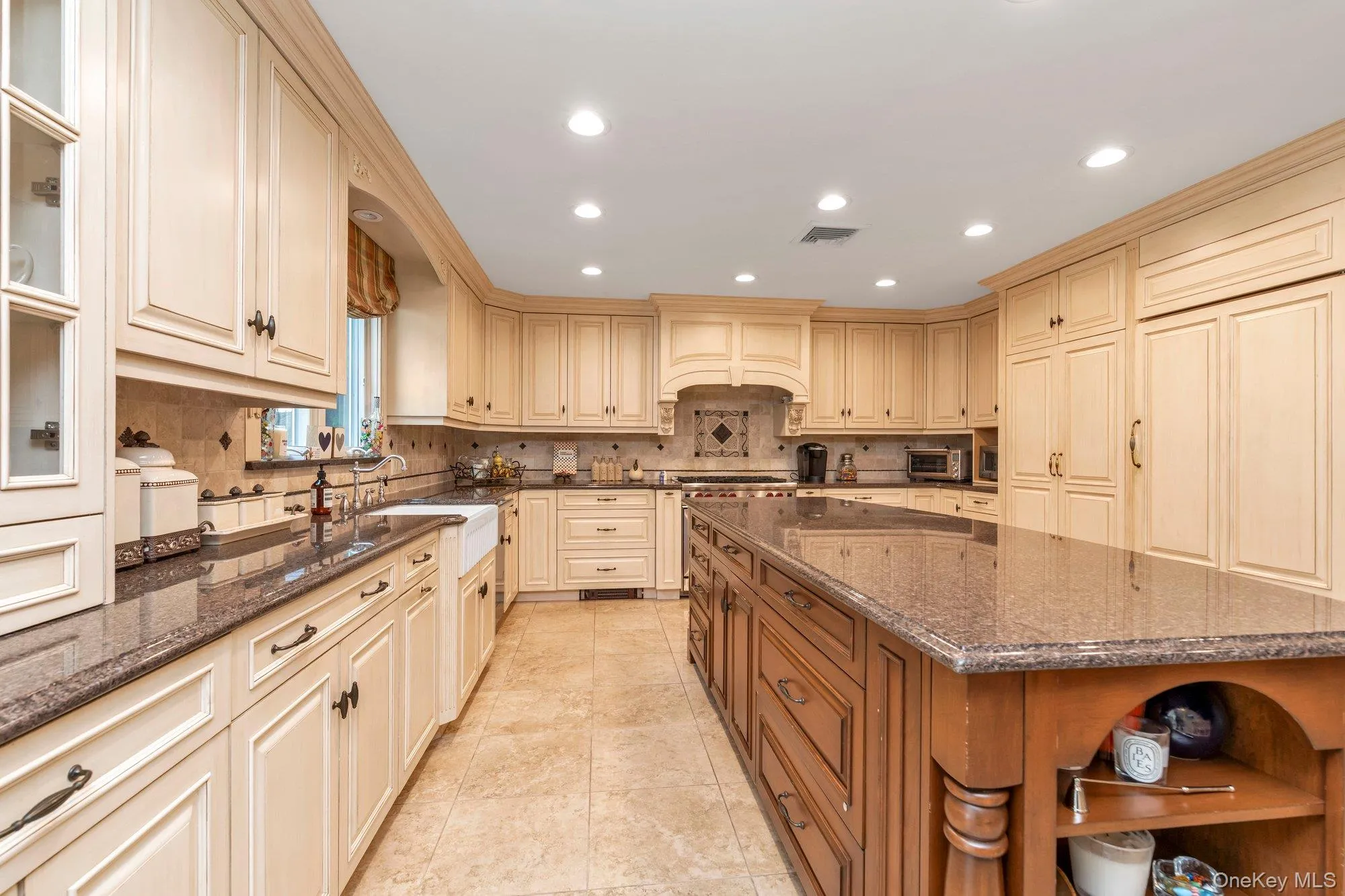 Gourmet kitchen featuring extensive cream-colored cabinetry, dark speckled countertops, a large center island with additional cabinetry, integrated appliances, and recessed lighting Gourmet kitchen featuring extensive cream-colored cabinetry, dark speckled countertops, a large center island with additional cabinetry, integrated appliances, and recessed lighting