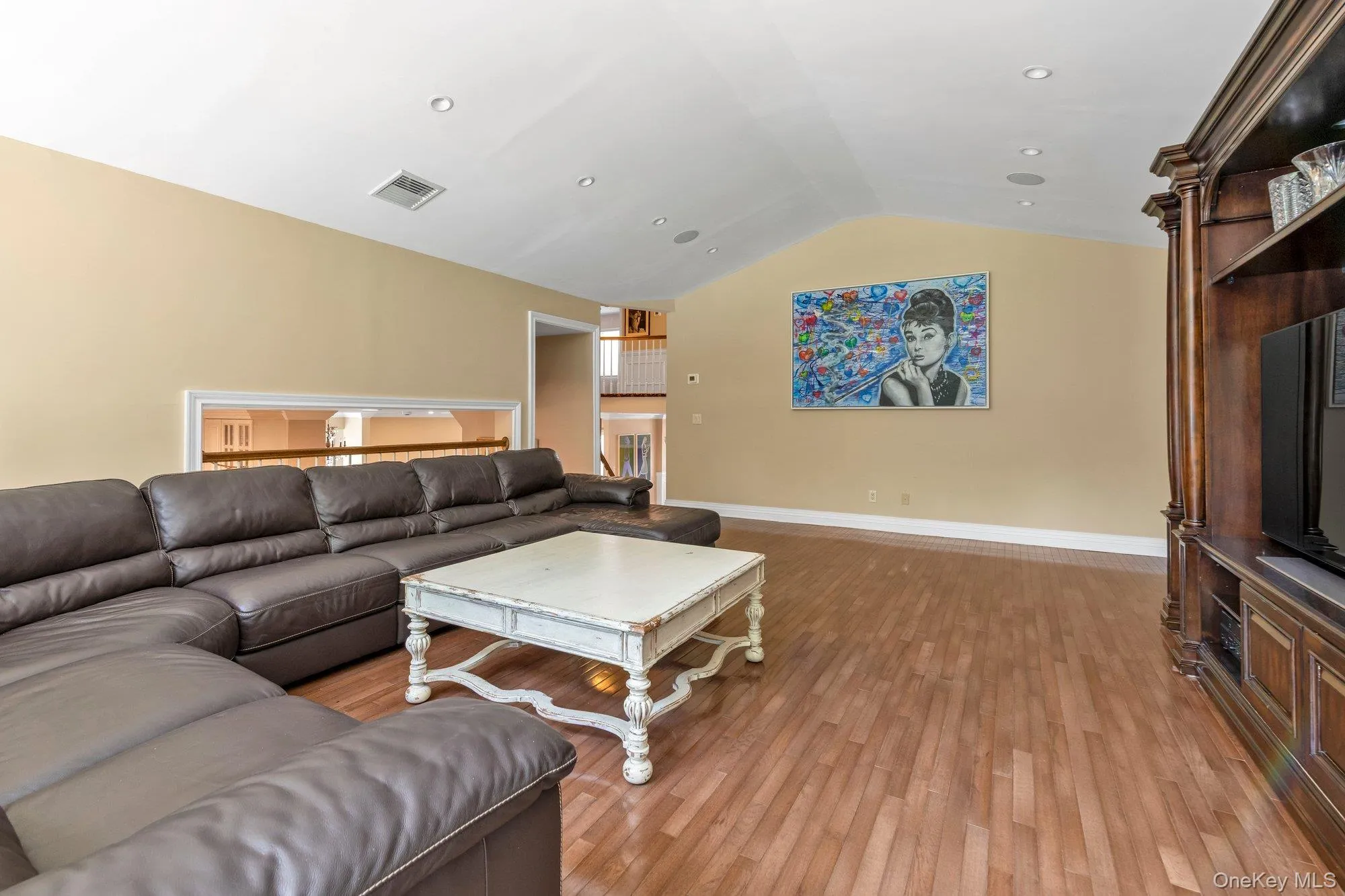 Spacious living area featuring wood-finish flooring, a vaulted ceiling, and recessed lighting Spacious living area featuring wood-finish flooring, a vaulted ceiling, and recessed lighting