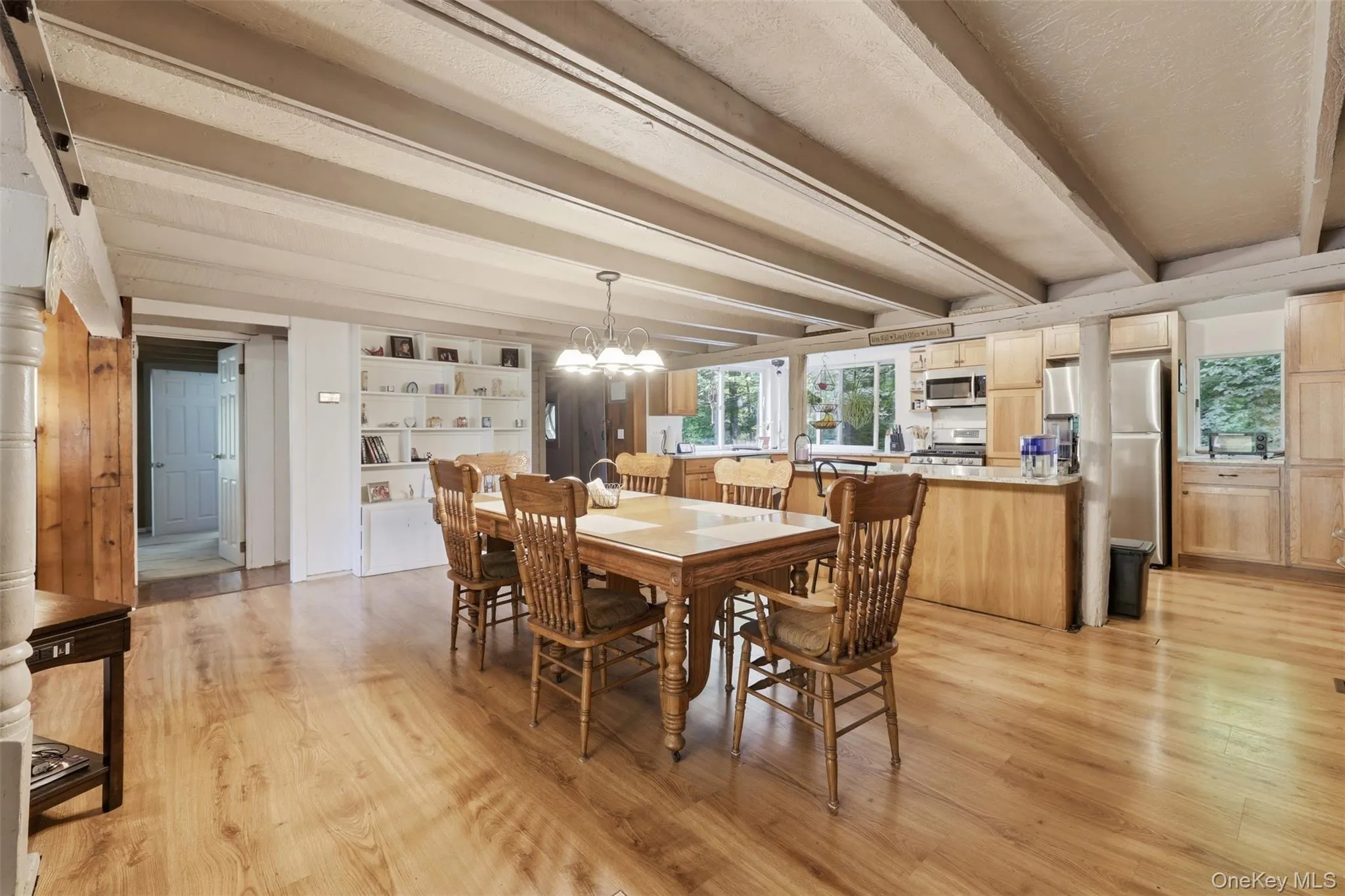Expansive open-concept dining room featuring wood-finish flooring, exposed ceiling beams, and chandelier Expansive open-concept dining room featuring wood-finish flooring, exposed ceiling beams, and chandelier