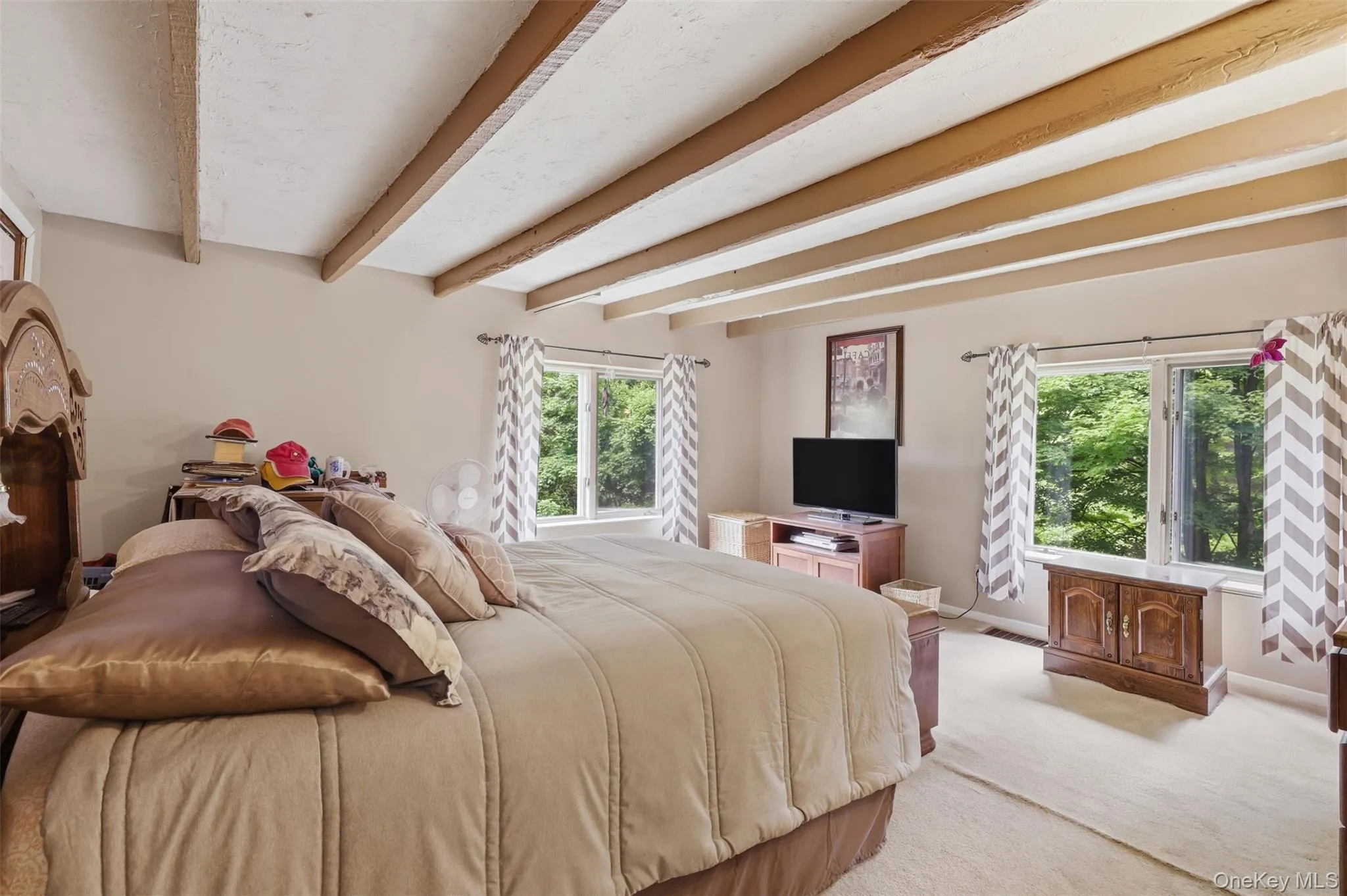 1st floor primary suite featuring exposed wood ceiling beams, neutral wall tones, and light-colored carpeting with closet on left side of bed and entrance to full bath on right side 1st floor primary suite featuring exposed wood ceiling beams, neutral wall tones, and light-colored carpeting with closet on left side of bed and entrance to full bath on right side