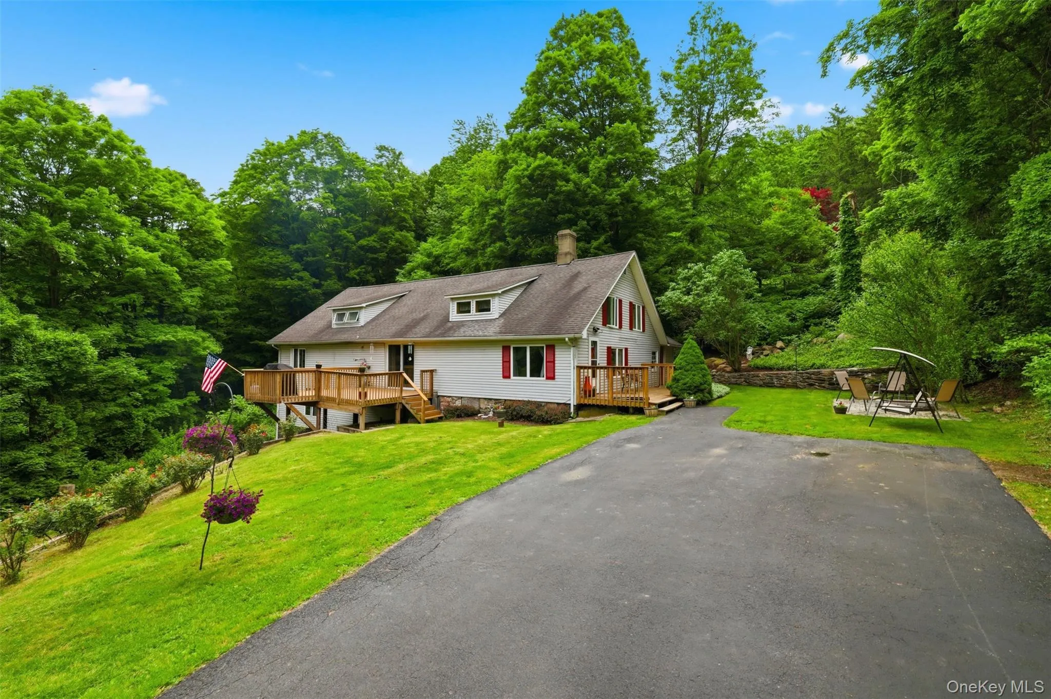 Residence featuring a white exterior with red shutters, a prominent wood deck, and a recently-sealed asphalt driveway Residence featuring a white exterior with red shutters, a prominent wood deck, and a recently-sealed asphalt driveway