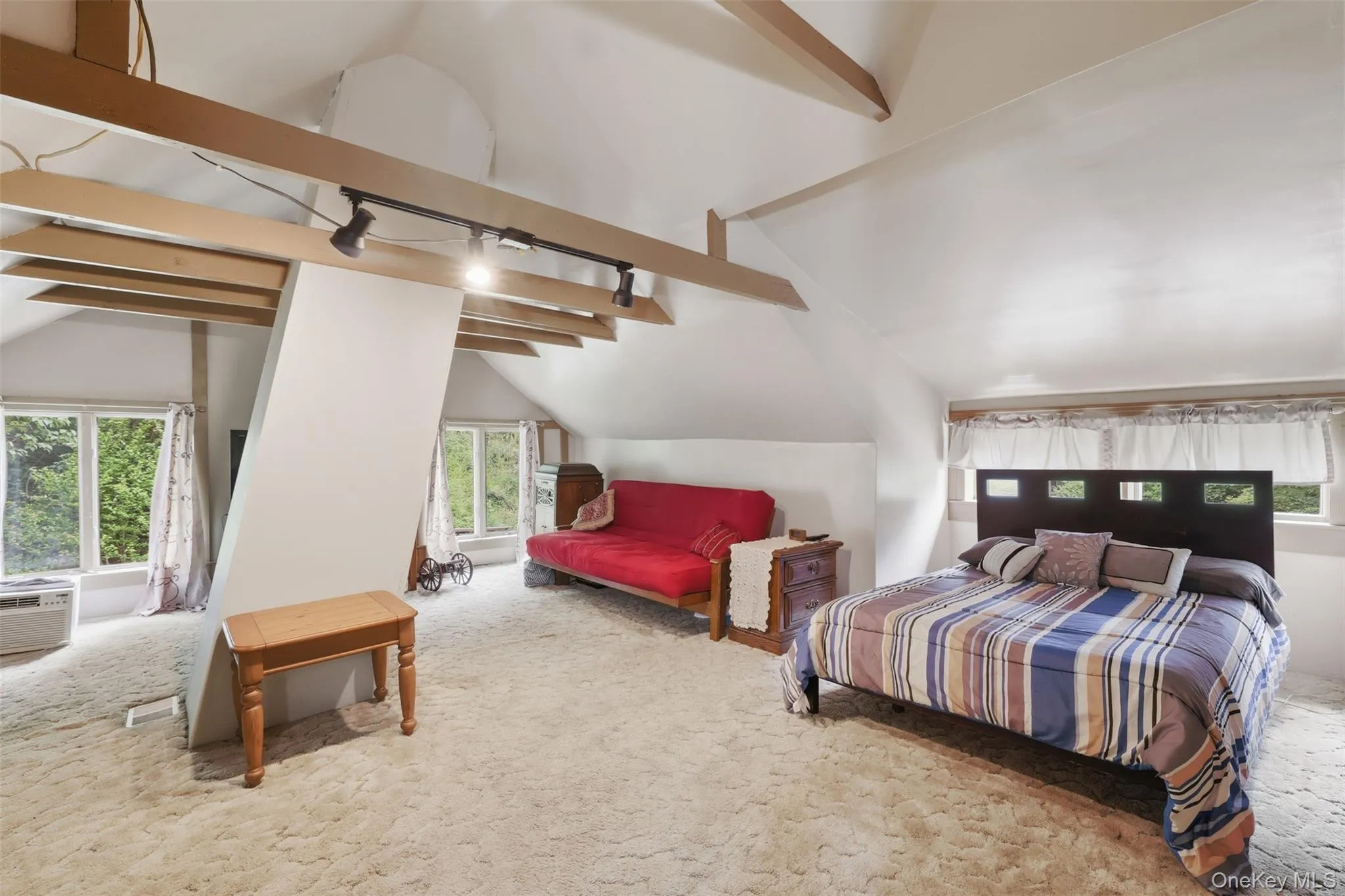 Large upstairs bonus room, guest room, or family room space featuring exposed ceiling beams, track lighting, and multiple windows with chimney Large upstairs bonus room, guest room, or family room space featuring exposed ceiling beams, track lighting, and multiple windows with chimney