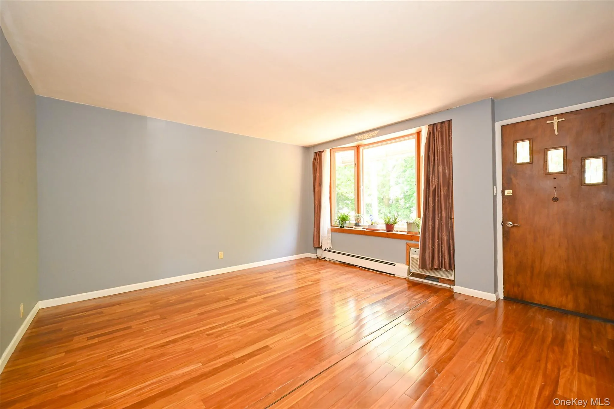 Spacious room with Pre-engineered hardwood flooring, light blue wall paint, and a large bay window with wood trim. Spacious room with Pre-engineered hardwood flooring, light blue wall paint, and a large bay window with wood trim.
