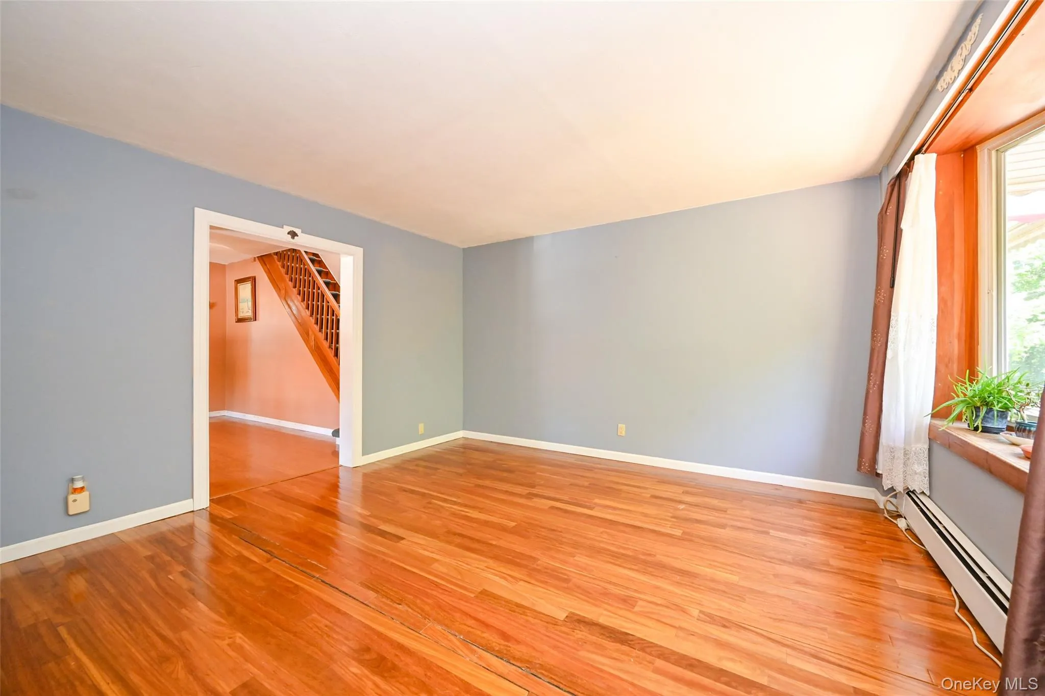 Spacious room with Pre-engineered hardwood flooring, light blue wall paint, and a large bay window with wood trim. Spacious room with Pre-engineered hardwood flooring, light blue wall paint, and a large bay window with wood trim.