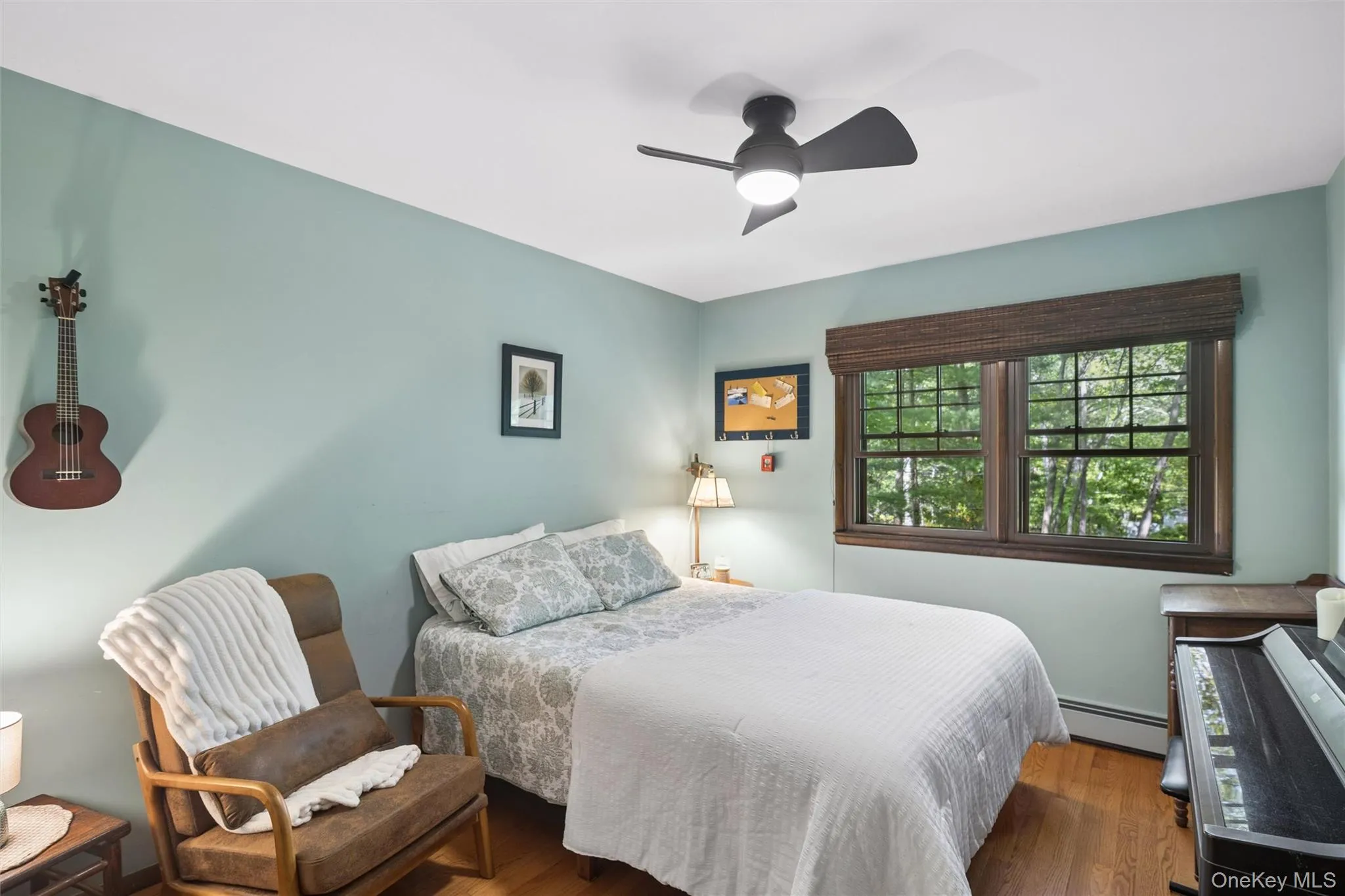 Bedroom featuring hardwood-finish flooring, a ceiling fan with integrated lighting, and a large window with wooden trim Bedroom featuring hardwood-finish flooring, a ceiling fan with integrated lighting, and a large window with wooden trim