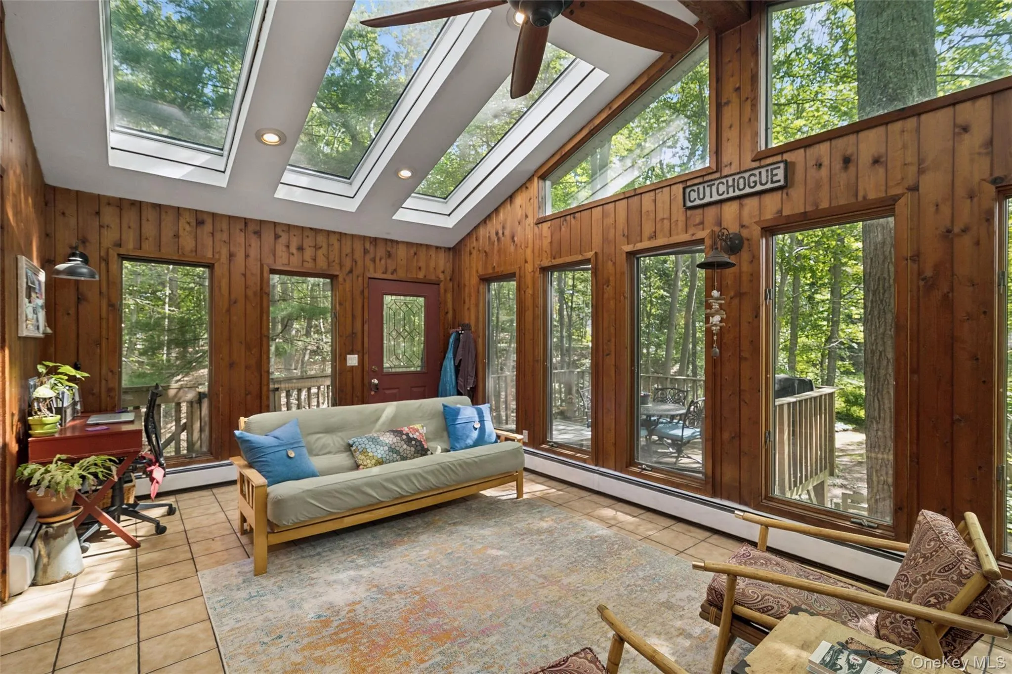 Sunroom featuring multiple skylights, wood paneling, tile flooring, a ceiling fan, and extensive window coverage Sunroom featuring multiple skylights, wood paneling, tile flooring, a ceiling fan, and extensive window coverage