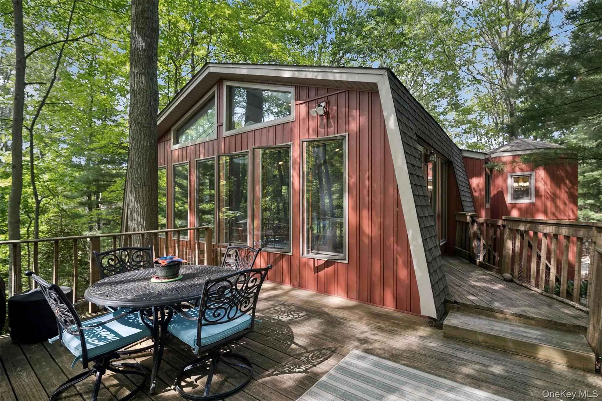 Wood-finish deck with railing extending around the structure, featuring a prominent sunroom with floor-to-ceiling windows and an angled roofline Wood-finish deck with railing extending around the structure, featuring a prominent sunroom with floor-to-ceiling windows and an angled roofline