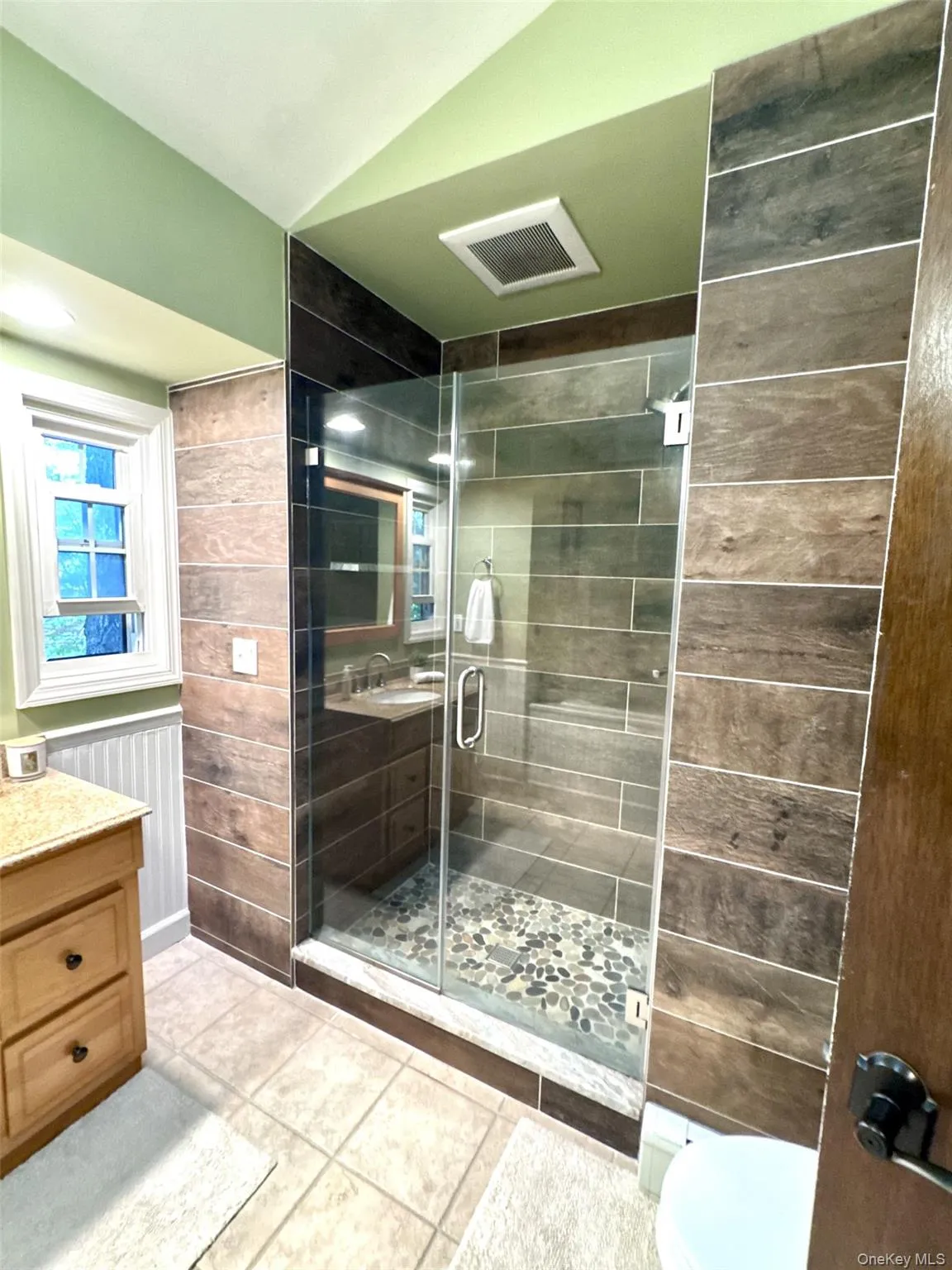 Bathroom featuring a frameless glass shower enclosure with pebble floor, wood-look tile surround, and an integrated bench Bathroom featuring a frameless glass shower enclosure with pebble floor, wood-look tile surround, and an integrated bench