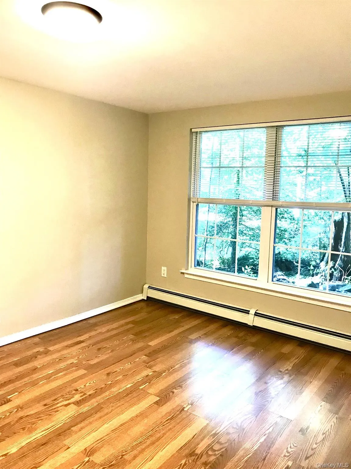 Wood-finish flooring with a natural grain, large window with blinds, baseboard heating, recessed lighting, and neutral wall paint Wood-finish flooring with a natural grain, large window with blinds, baseboard heating, recessed lighting, and neutral wall paint