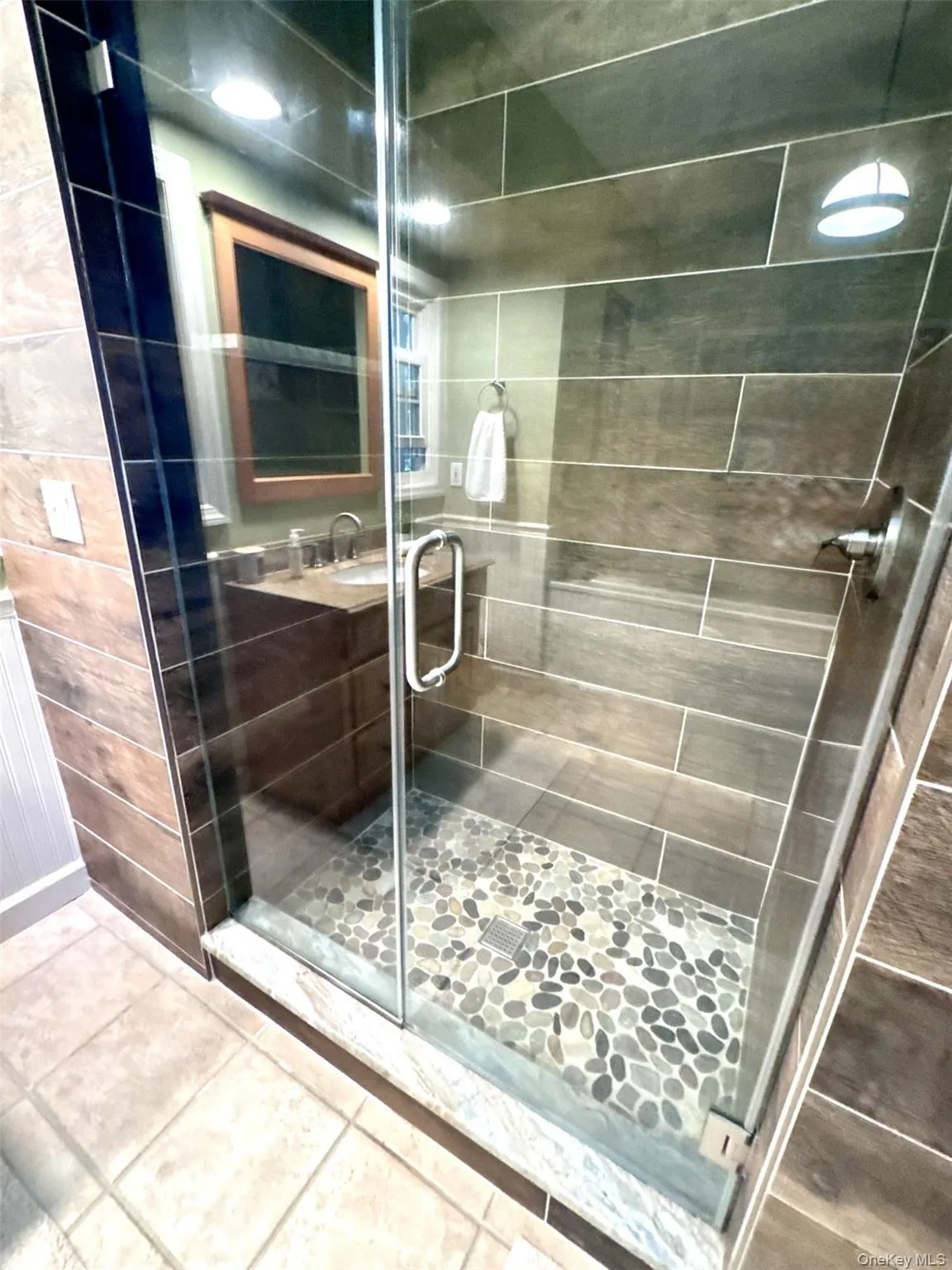 Glass-enclosed shower featuring pebble-style flooring, large format wall tiling, and a brushed nickel shower fixture Glass-enclosed shower featuring pebble-style flooring, large format wall tiling, and a brushed nickel shower fixture