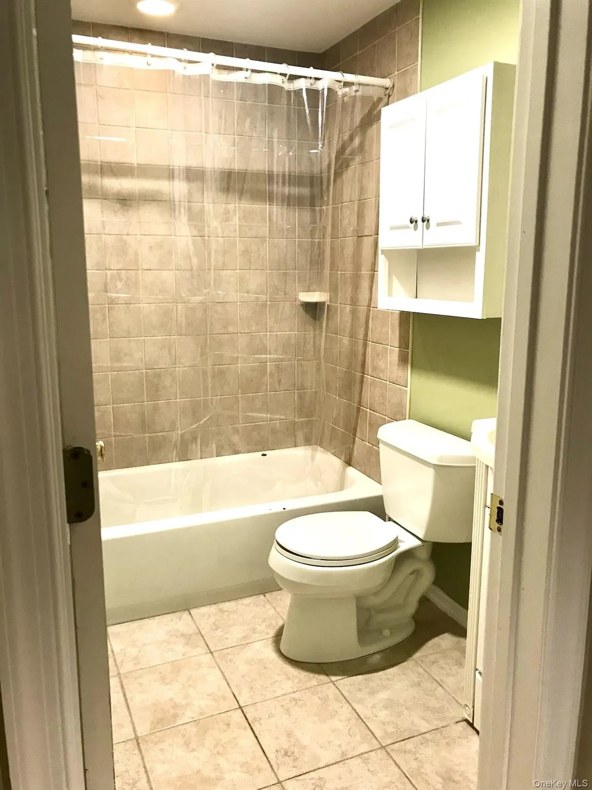 Bathroom featuring a white bathtub, ceramic tile flooring, and a wall-mounted storage cabinet Bathroom featuring a white bathtub, ceramic tile flooring, and a wall-mounted storage cabinet