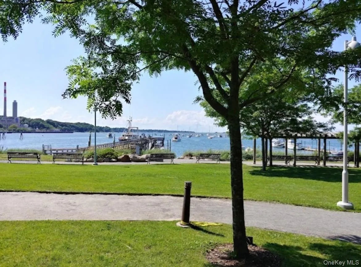 Expansive green space featuring a paved pathway, mature trees, and a waterfront setting with boats in the distance Expansive green space featuring a paved pathway, mature trees, and a waterfront setting with boats in the distance