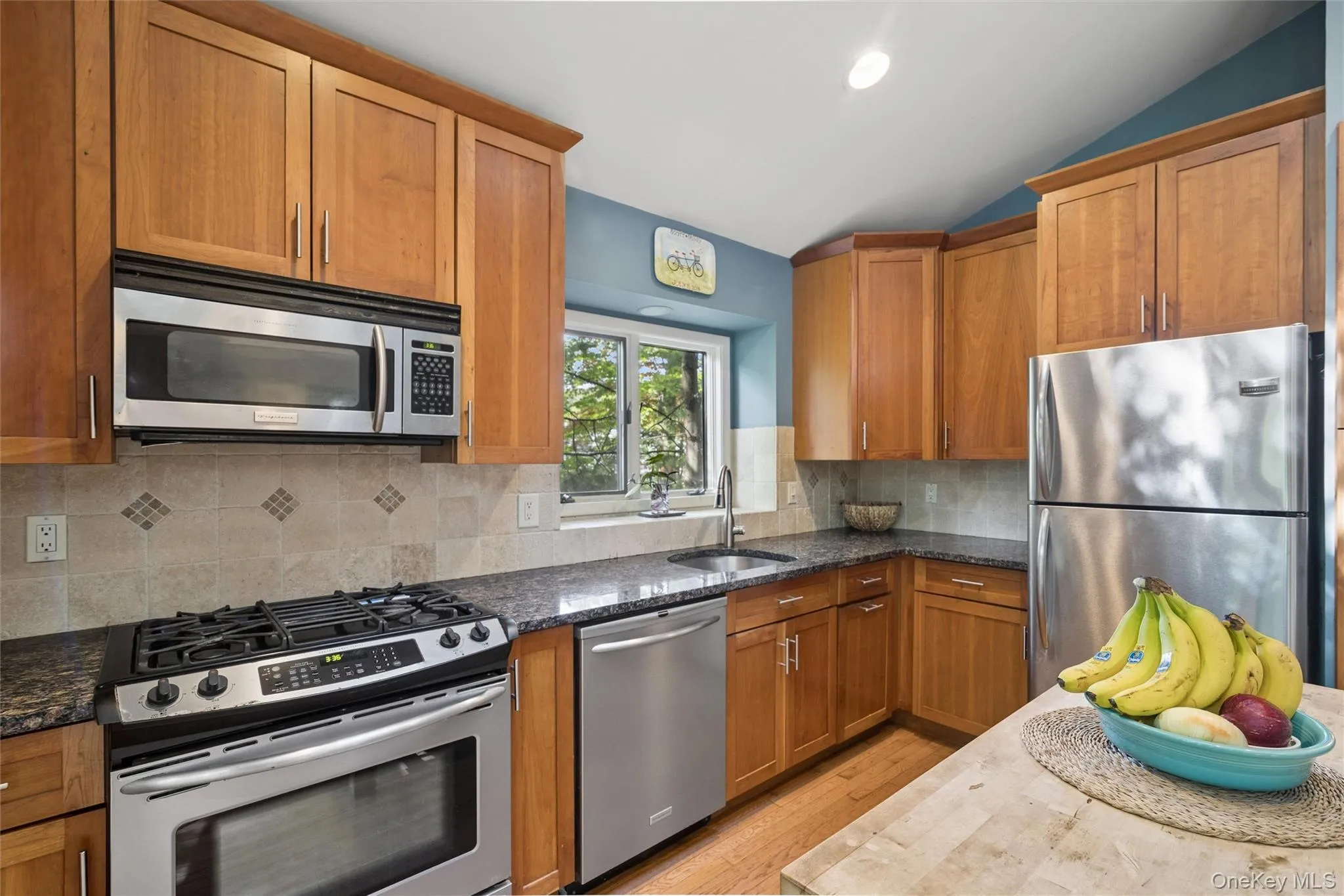Kitchen featuring wood-finish cabinetry, stainless steel appliances, speckled stone countertops, and a tiled backsplash Kitchen featuring wood-finish cabinetry, stainless steel appliances, speckled stone countertops, and a tiled backsplash