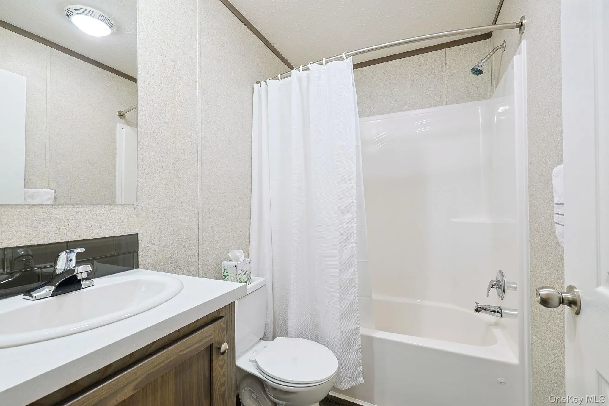 Bathroom featuring a white integrated sink with a chrome faucet, a dark wood-finish vanity, and a white shower-over-tub combination with a curved shower rod Bathroom featuring a white integrated sink with a chrome faucet, a dark wood-finish vanity, and a white shower-over-tub combination with a curved shower rod