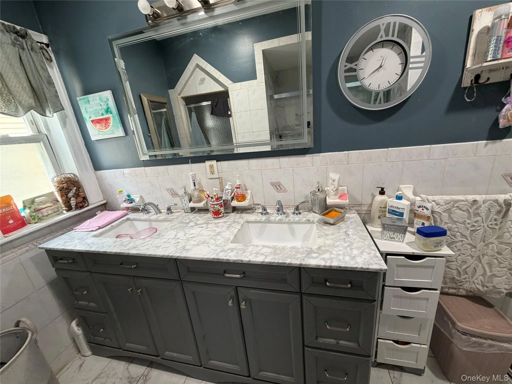 Double vanity featuring a white marble-patterned countertop, dual integrated sinks, and gray cabinetry with brushed nickel hardware Double vanity featuring a white marble-patterned countertop, dual integrated sinks, and gray cabinetry with brushed nickel hardware