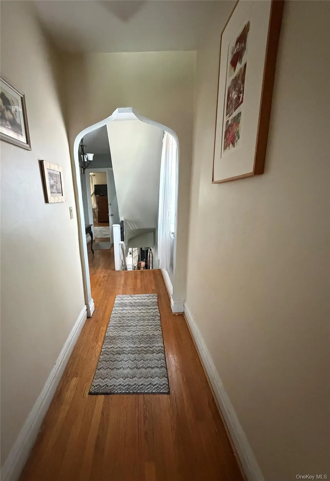 Hardwood flooring in a neutral-toned hallway with crown molding and an arched doorway Hardwood flooring in a neutral-toned hallway with crown molding and an arched doorway