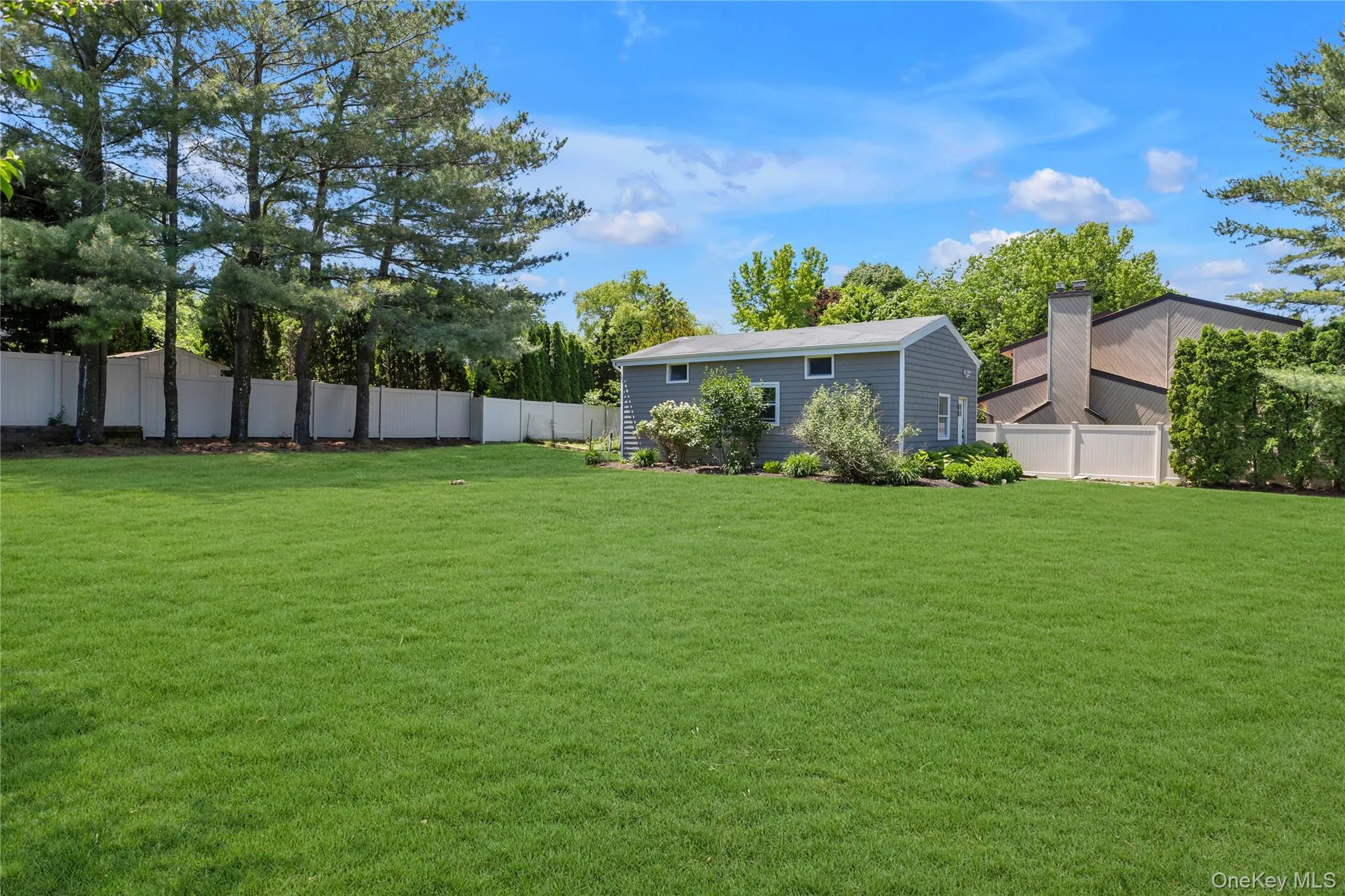 Expansive green lawn with a white privacy fence and mature perimeter trees Expansive green lawn with a white privacy fence and mature perimeter trees