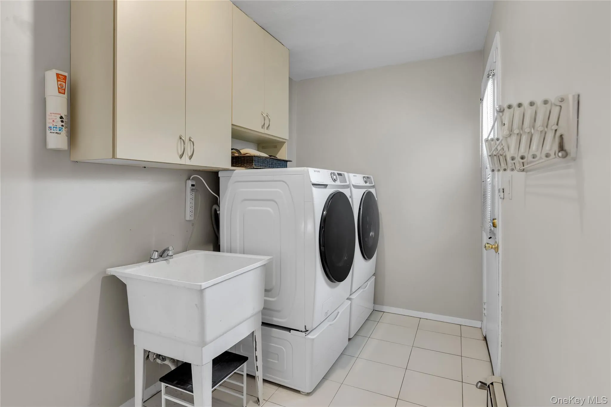 Utility room featuring a laundry sink, overhead cabinetry, and tile flooring Utility room featuring a laundry sink, overhead cabinetry, and tile flooring