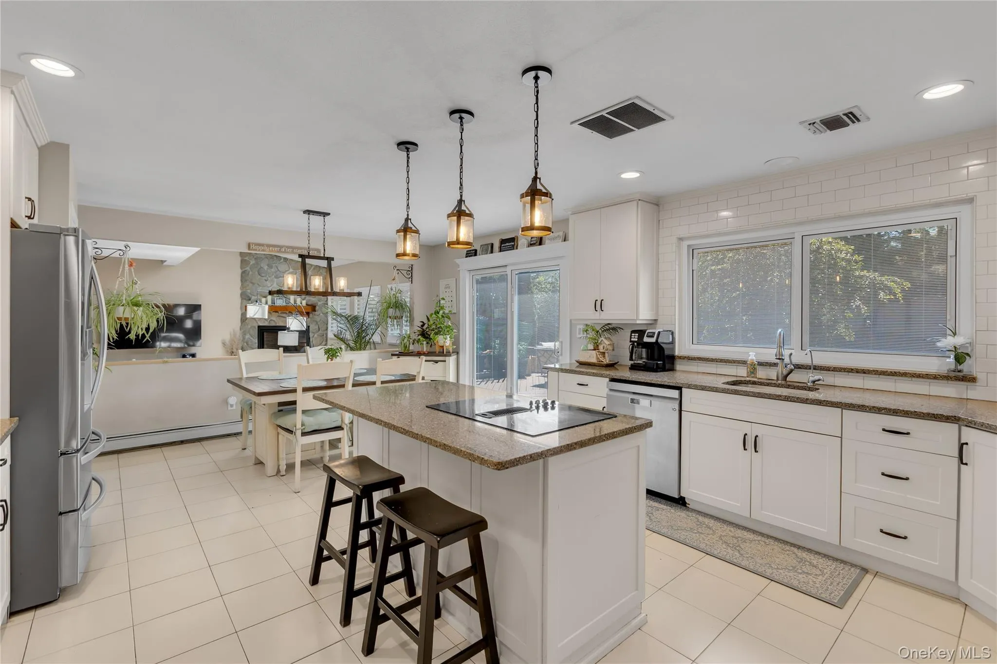 Bright kitchen featuring white cabinetry, a center island with a cooktop, granite countertops, and tile flooring Bright kitchen featuring white cabinetry, a center island with a cooktop, granite countertops, and tile flooring
